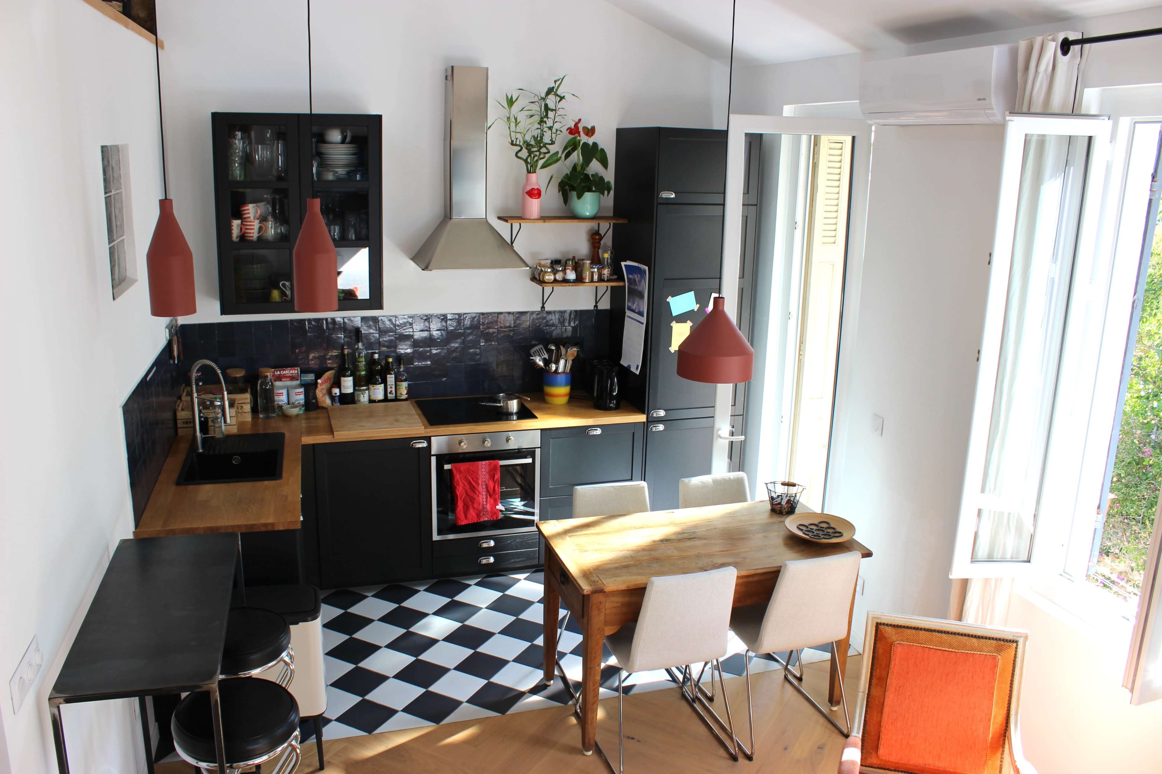 The image shows a modern kitchen with a dining table, sleek cabinetry, and a checkered floor layout.