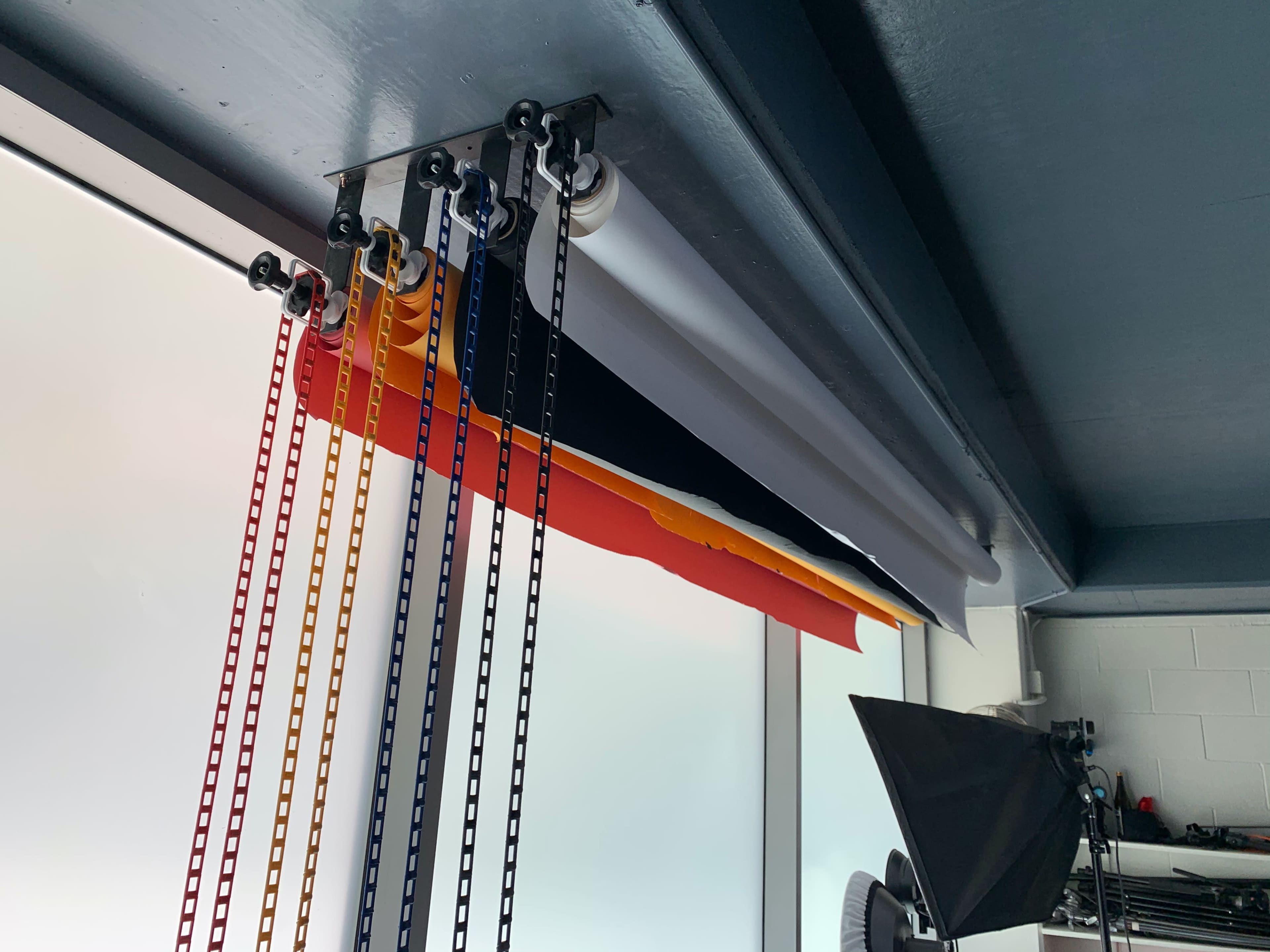 A curtain system with multiple colored rolls of fabric is mounted on a ceiling track above large windows.