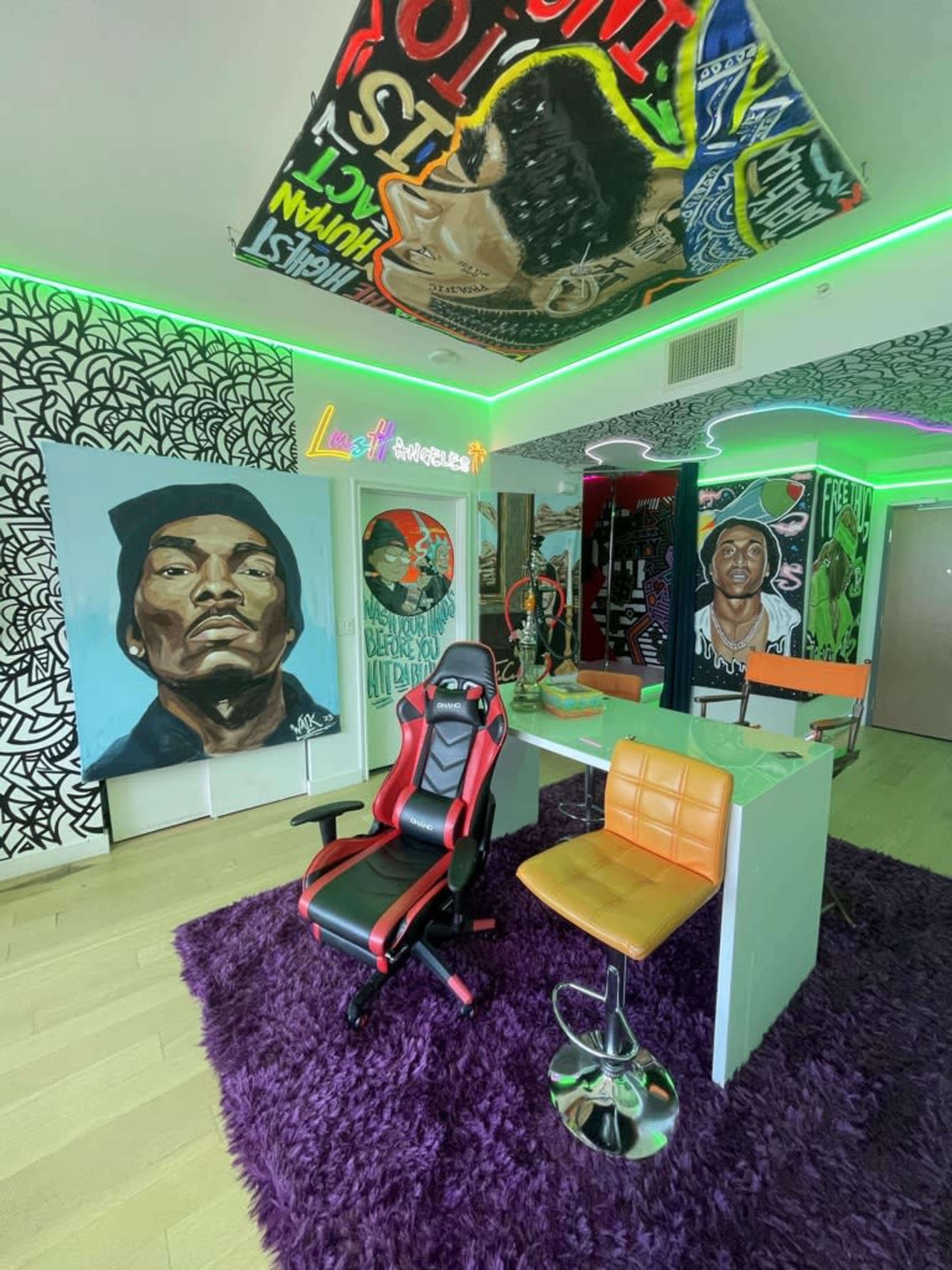 The image depicts a modern, vibrant workspace featuring colorful graffiti art on the walls, a plush purple rug, and stylish furniture including a red and black gaming chair and an orange bar stool.