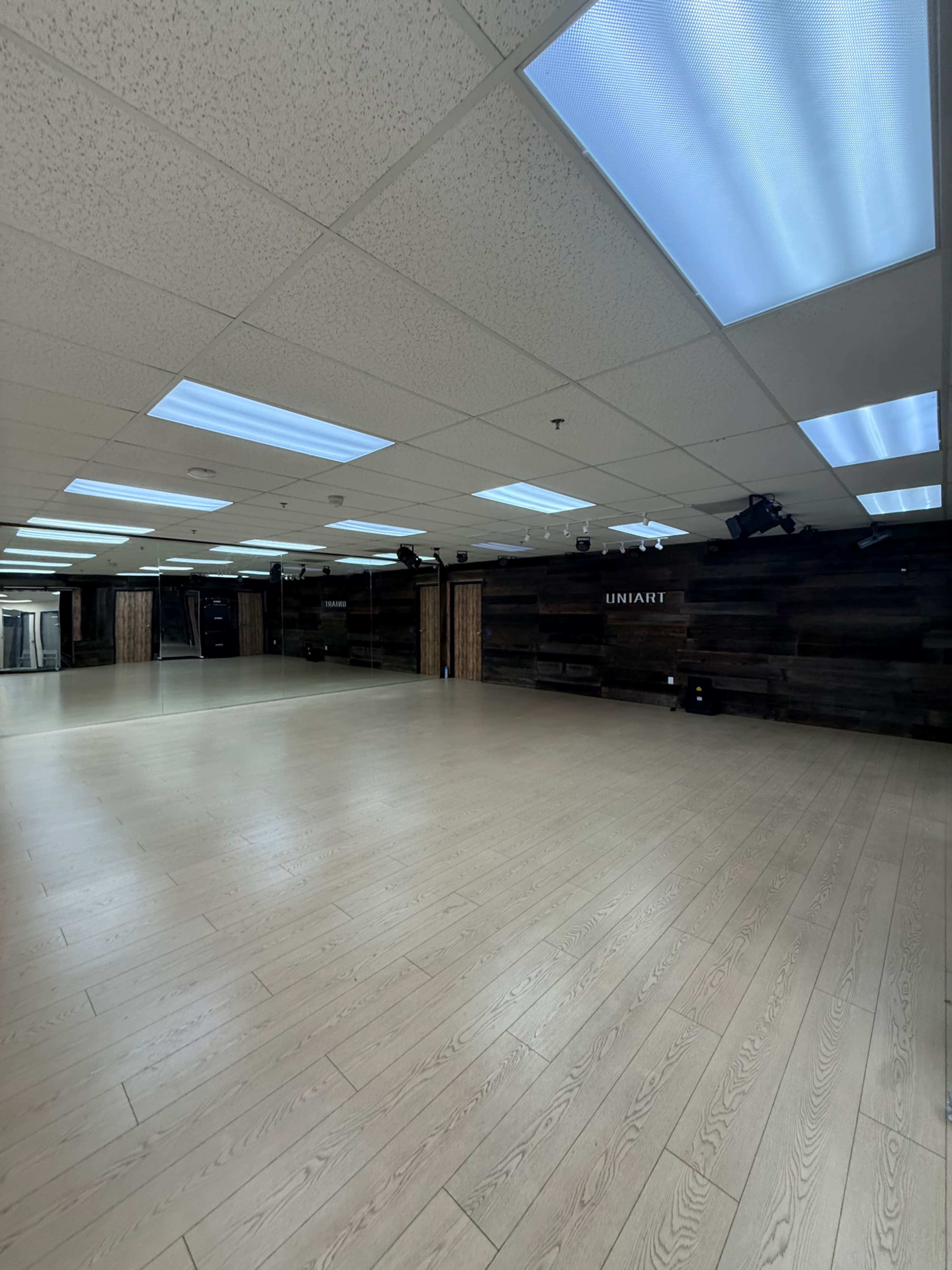 The image shows an empty studio space with wooden walls, large windows, and overhead fluorescent lighting.
