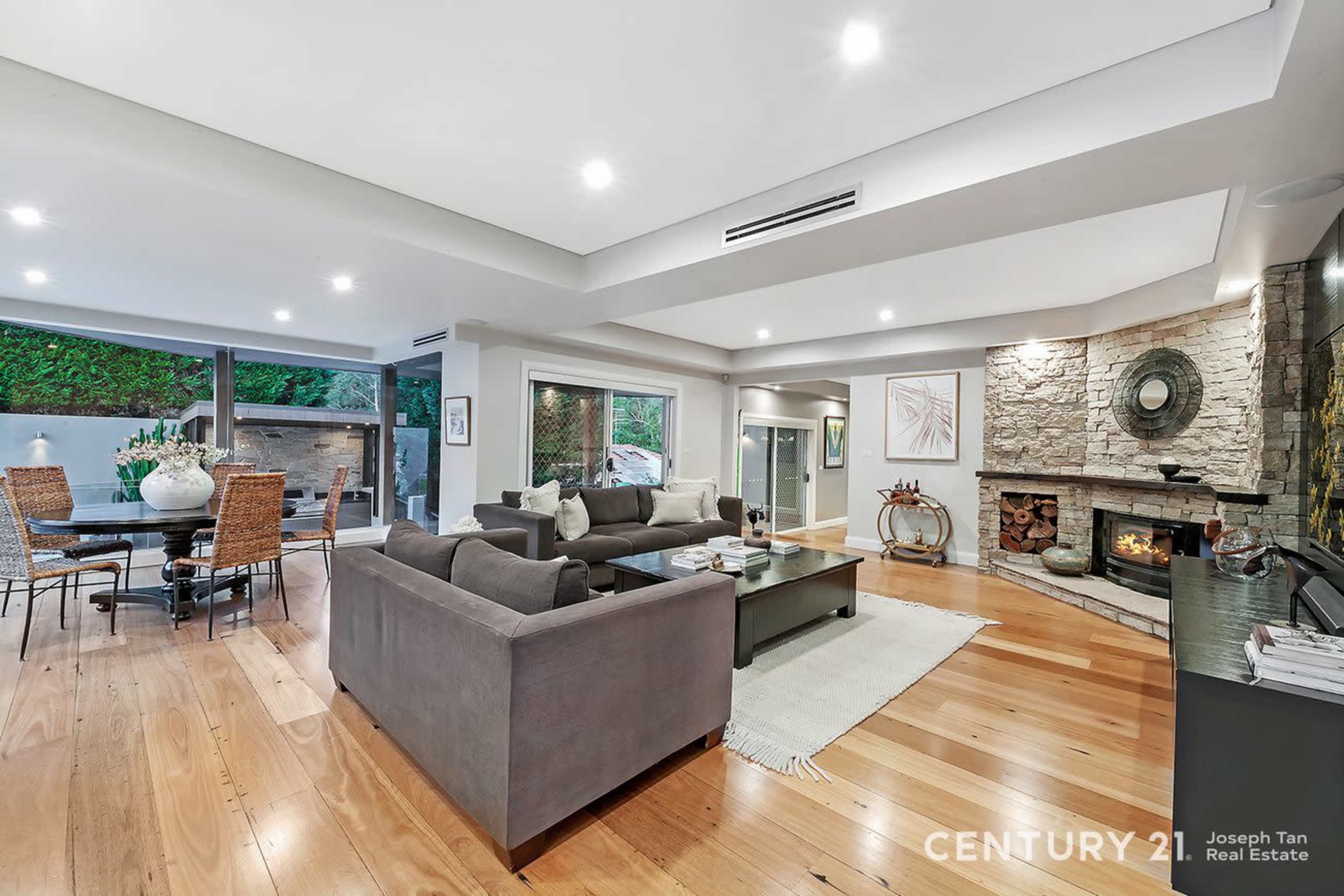 The image shows a modern living room and dining area with hardwood floors, large windows, and a stone fireplace.