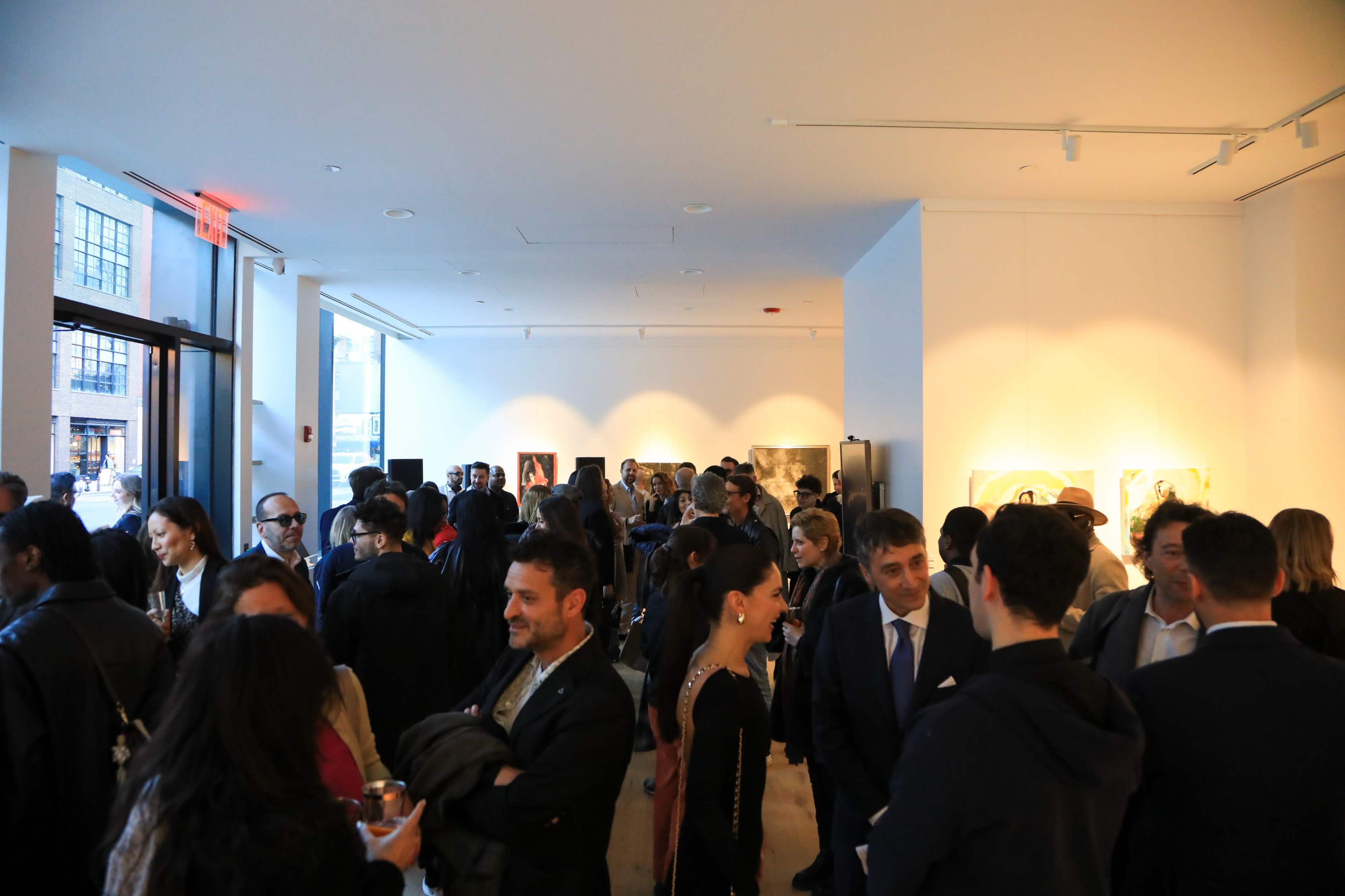 A large group of people is mingling and conversing in a brightly lit art gallery.