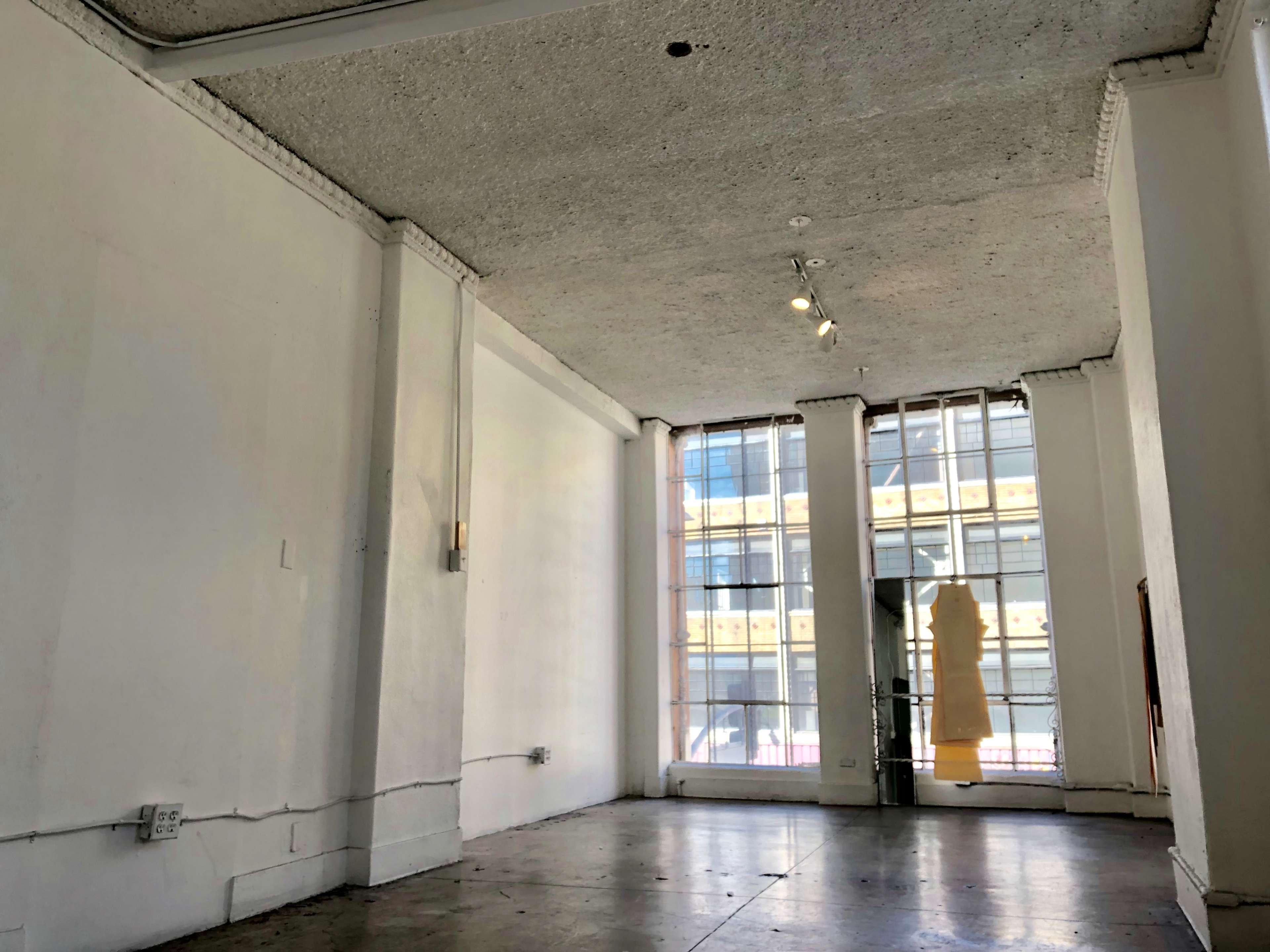 An empty room with a textured ceiling, large windows, and concrete flooring.
