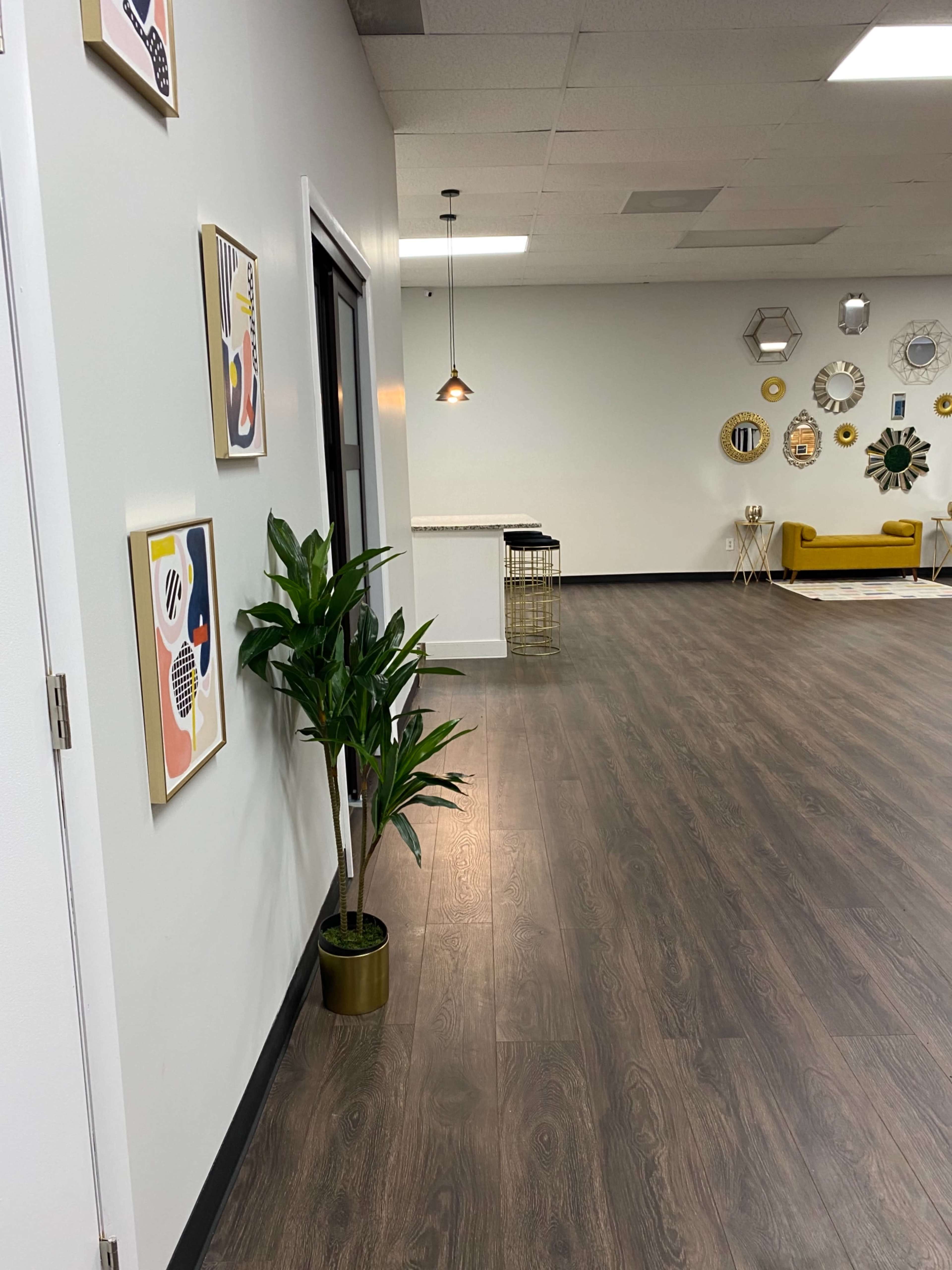 A large, modern interior features a long, open space with wooden flooring, decorative wall art, a potted plant, and a seating area against a wall with circular decorations.