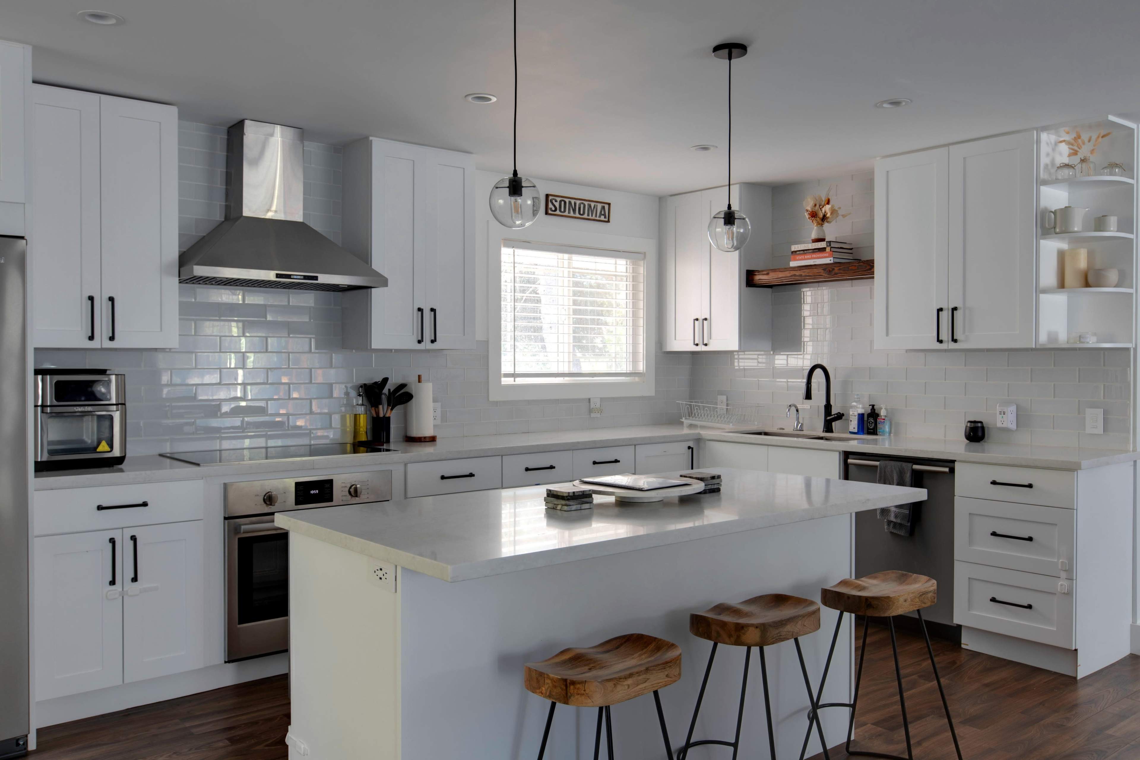 A modern kitchen with white cabinets, stainless steel appliances, and an island with wooden stools.