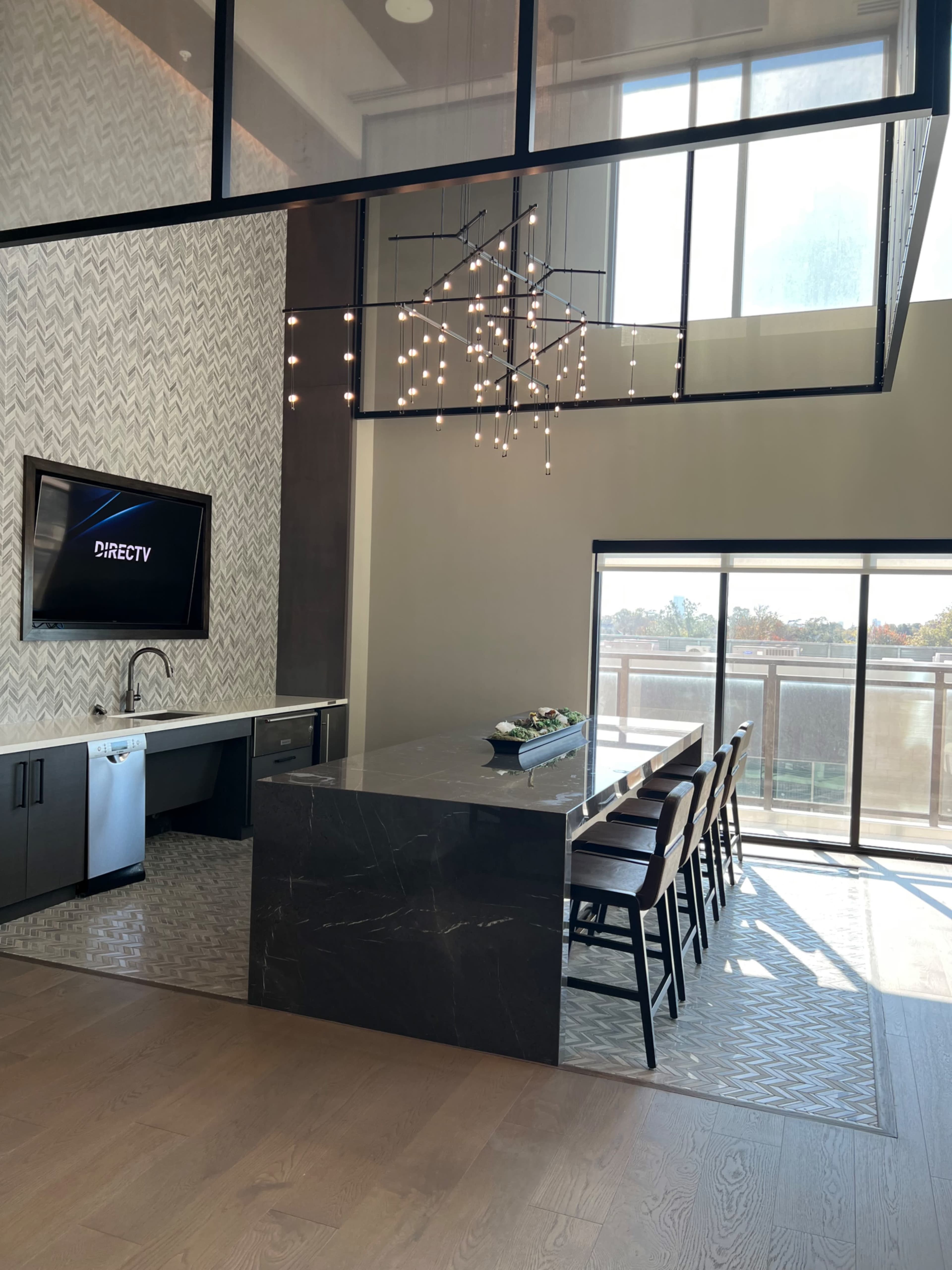 A modern kitchen features a large dark island with seating and a dining area next to large windows, providing natural light.