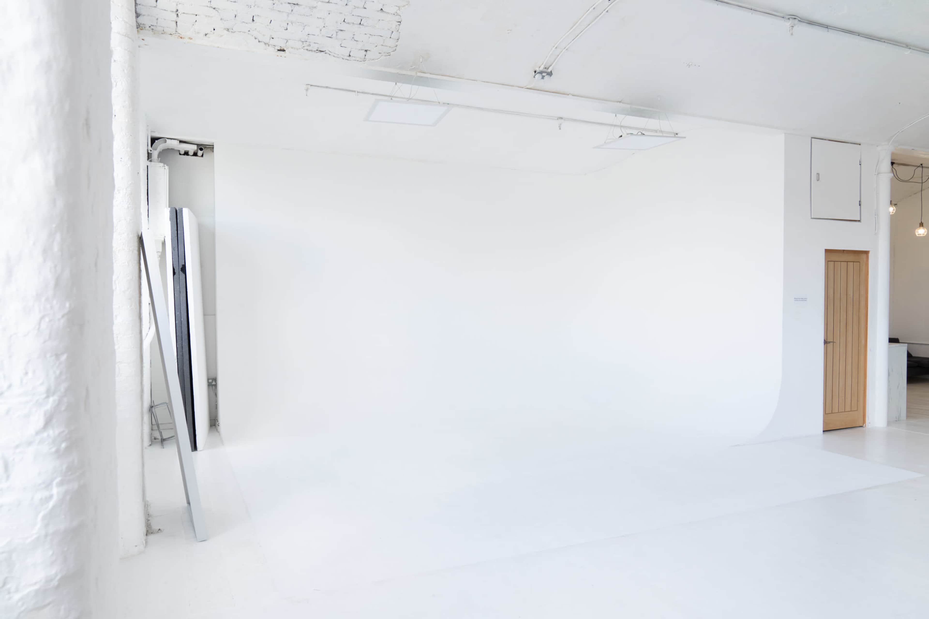 A spacious, minimalist studio with a white backdrop and a wooden door.