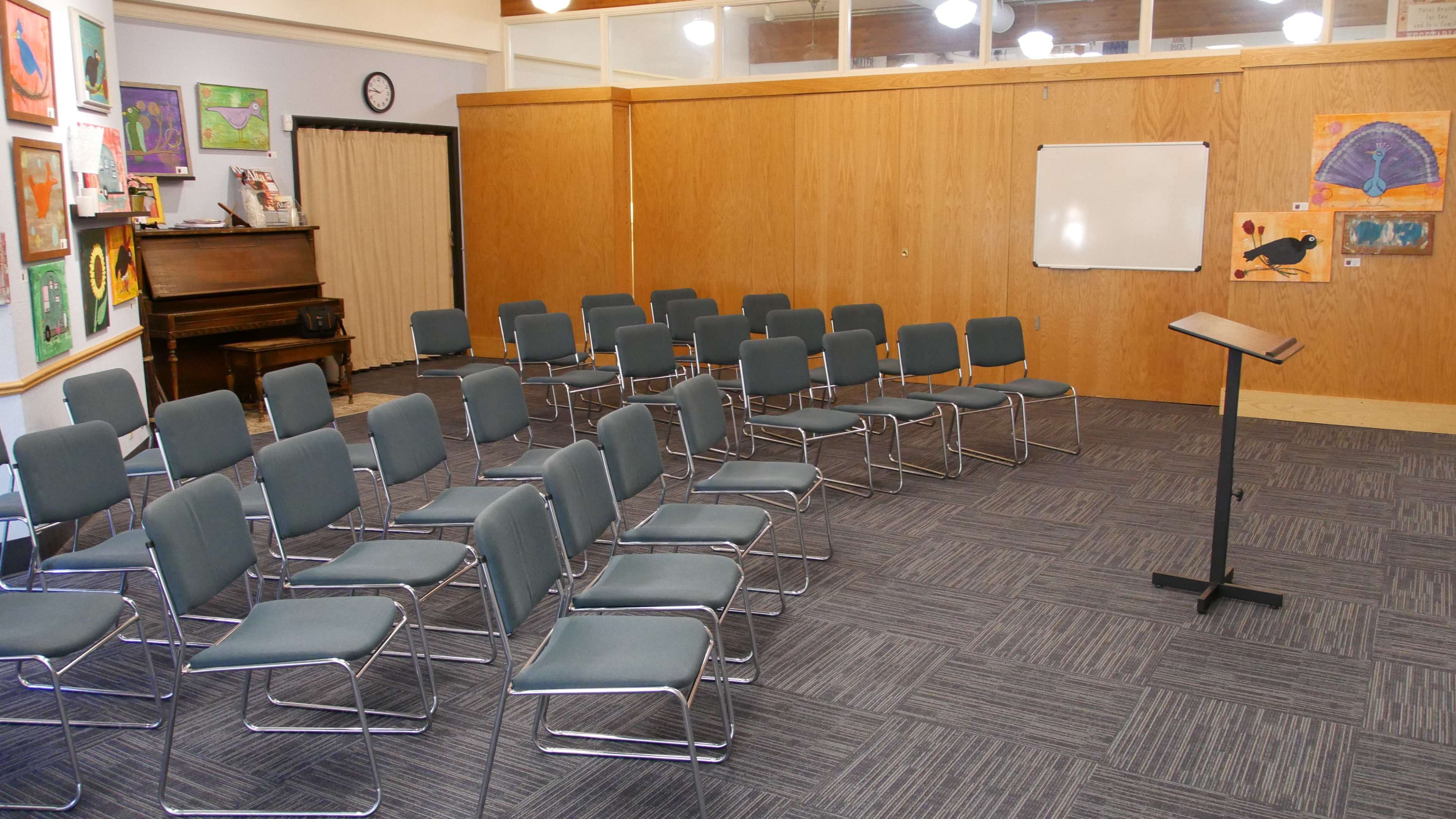 A room with neatly arranged gray chairs facing a podium, accompanied by colorful artwork on the walls.