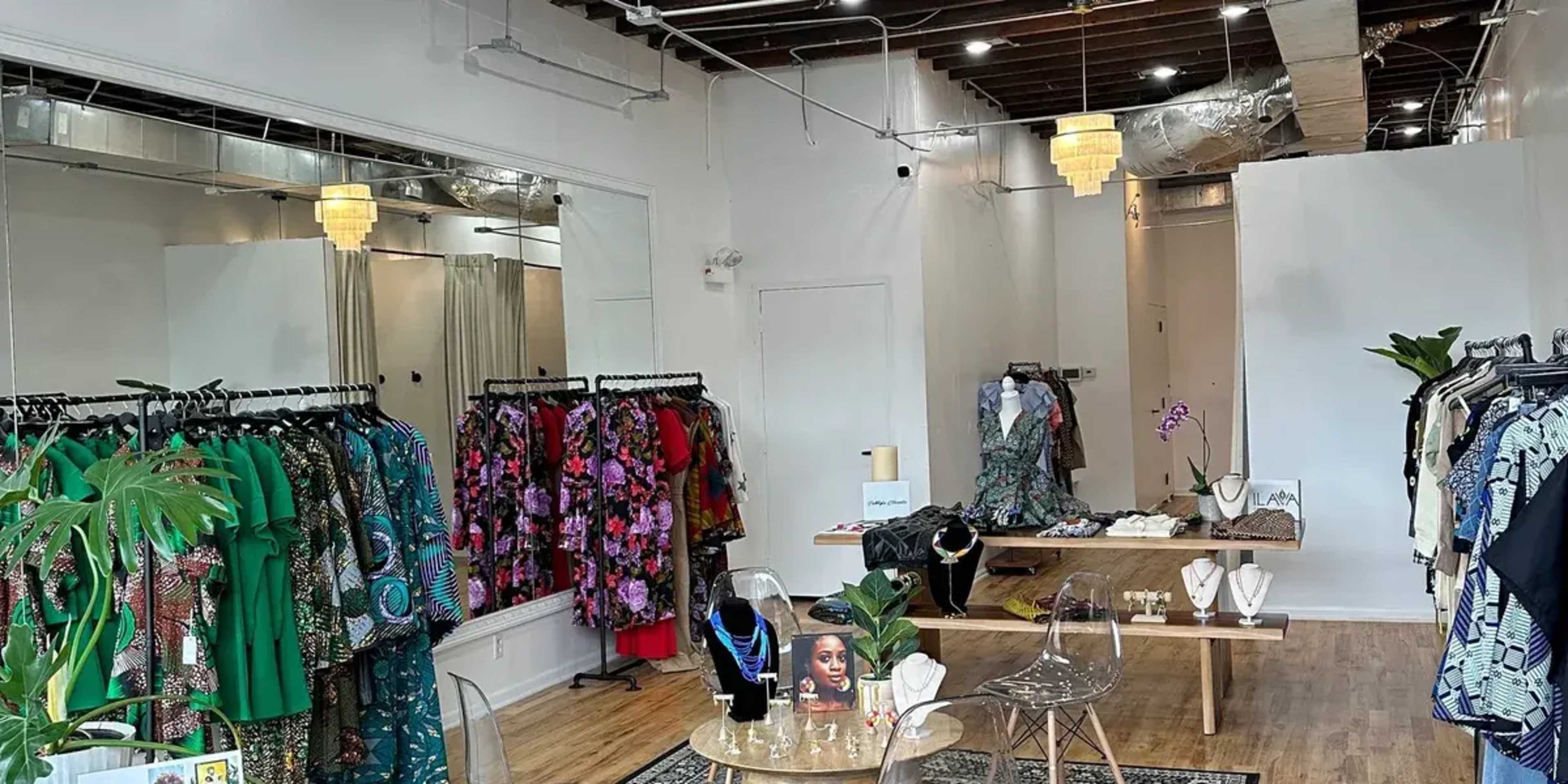 The image shows an interior of a clothing boutique featuring racks of colorful dresses, a display table with jewelry, and mirrors on the walls.