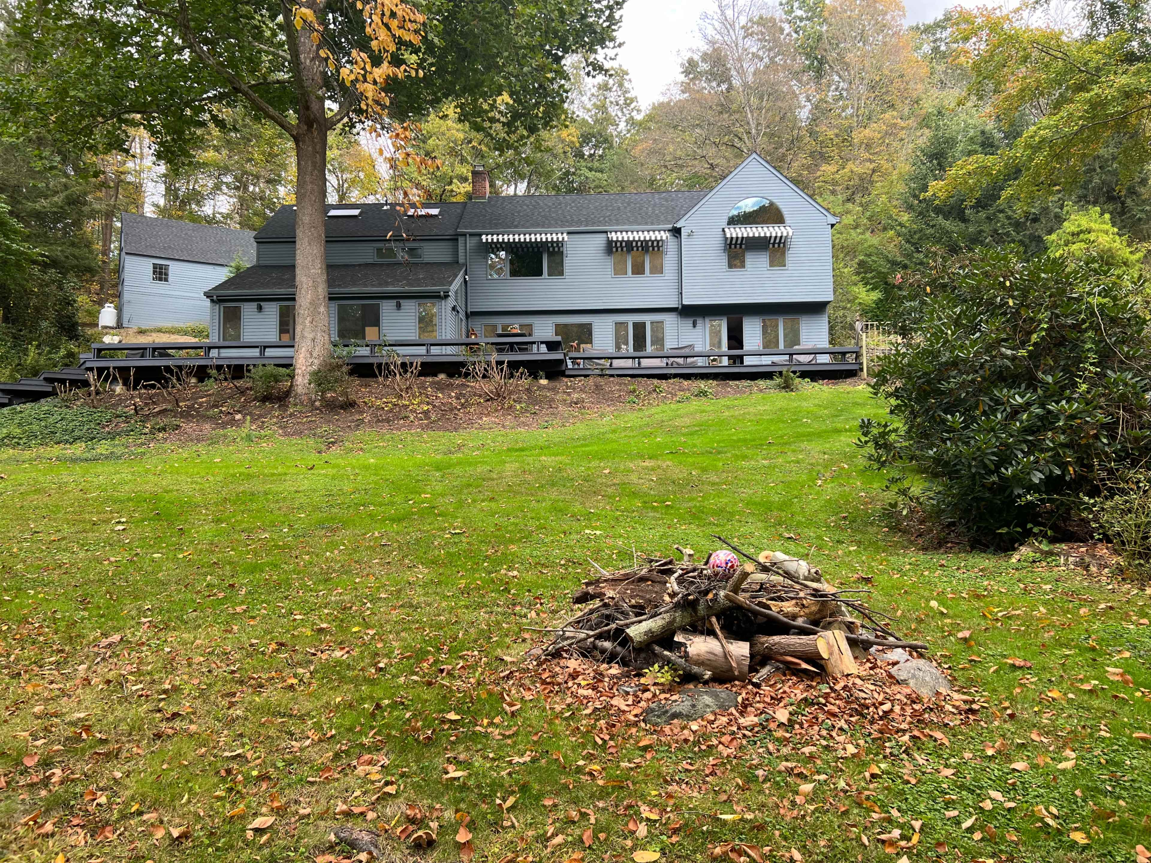 A large blue house with multiple windows and a porch is located behind a grassy area featuring a fire pit made of logs and stones.