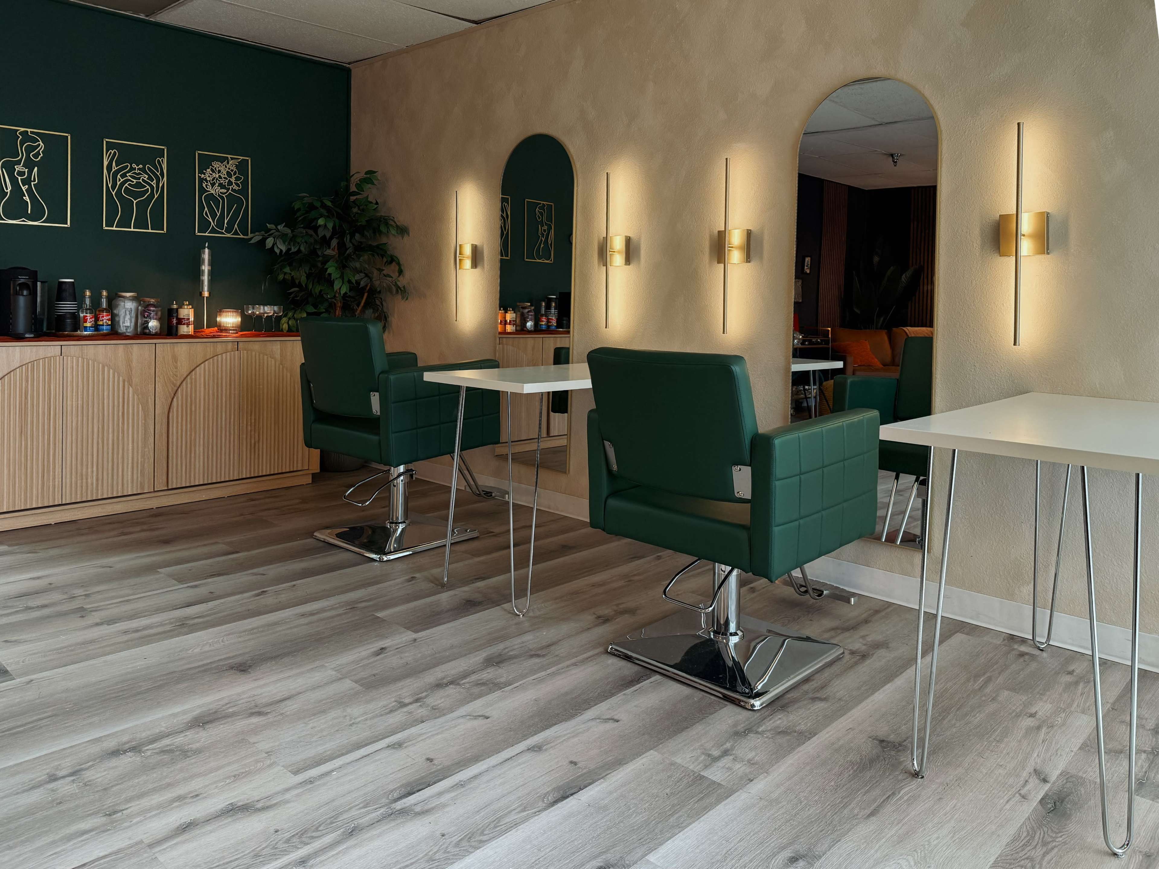 The image shows a modern interior of a salon with green chairs, white tables, and decorative mirrors against a neutral-colored wall.