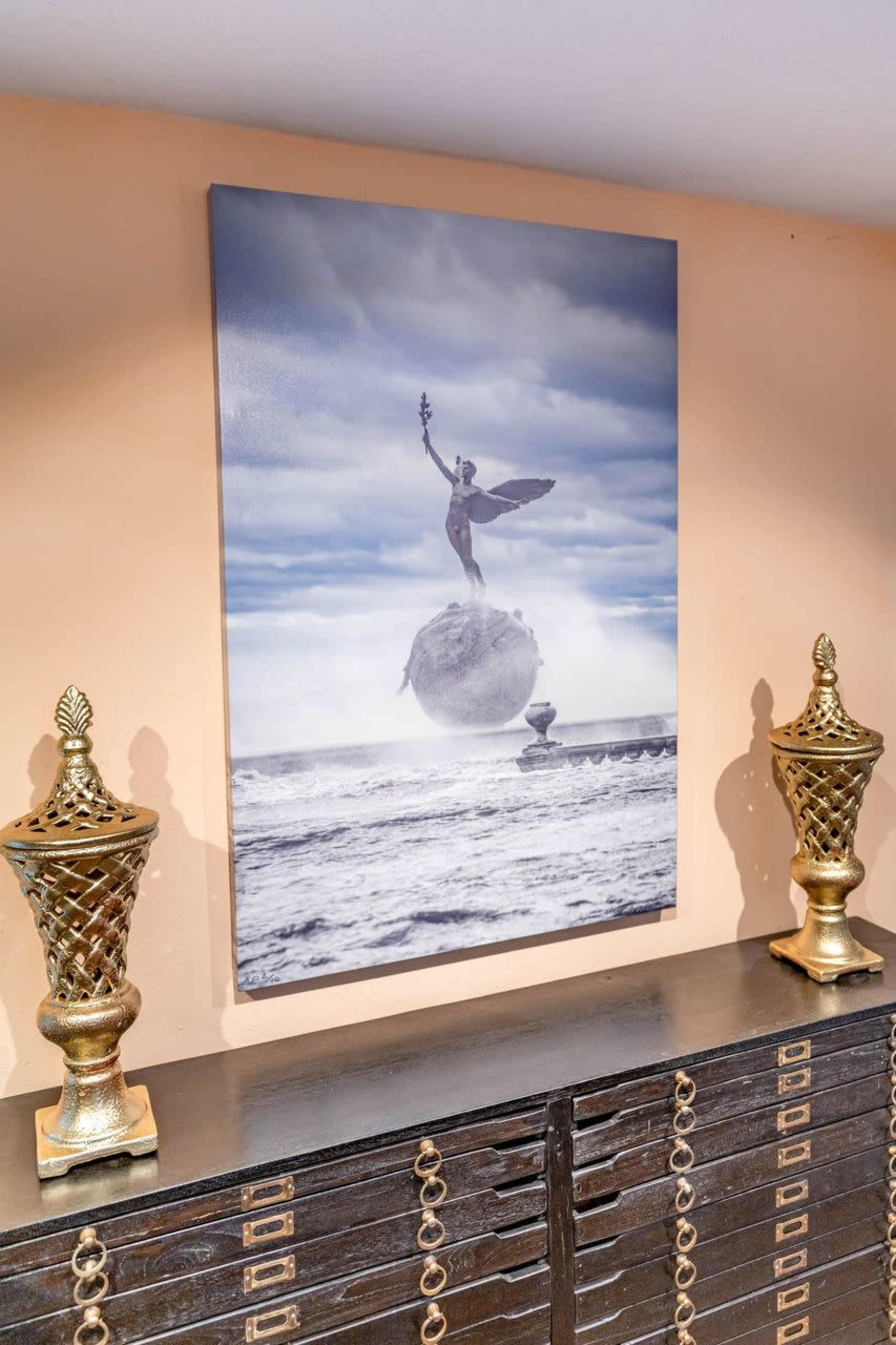 A large painting of a statue holding a staff while balancing on a sphere is displayed on a wall above two decorative golden urns.