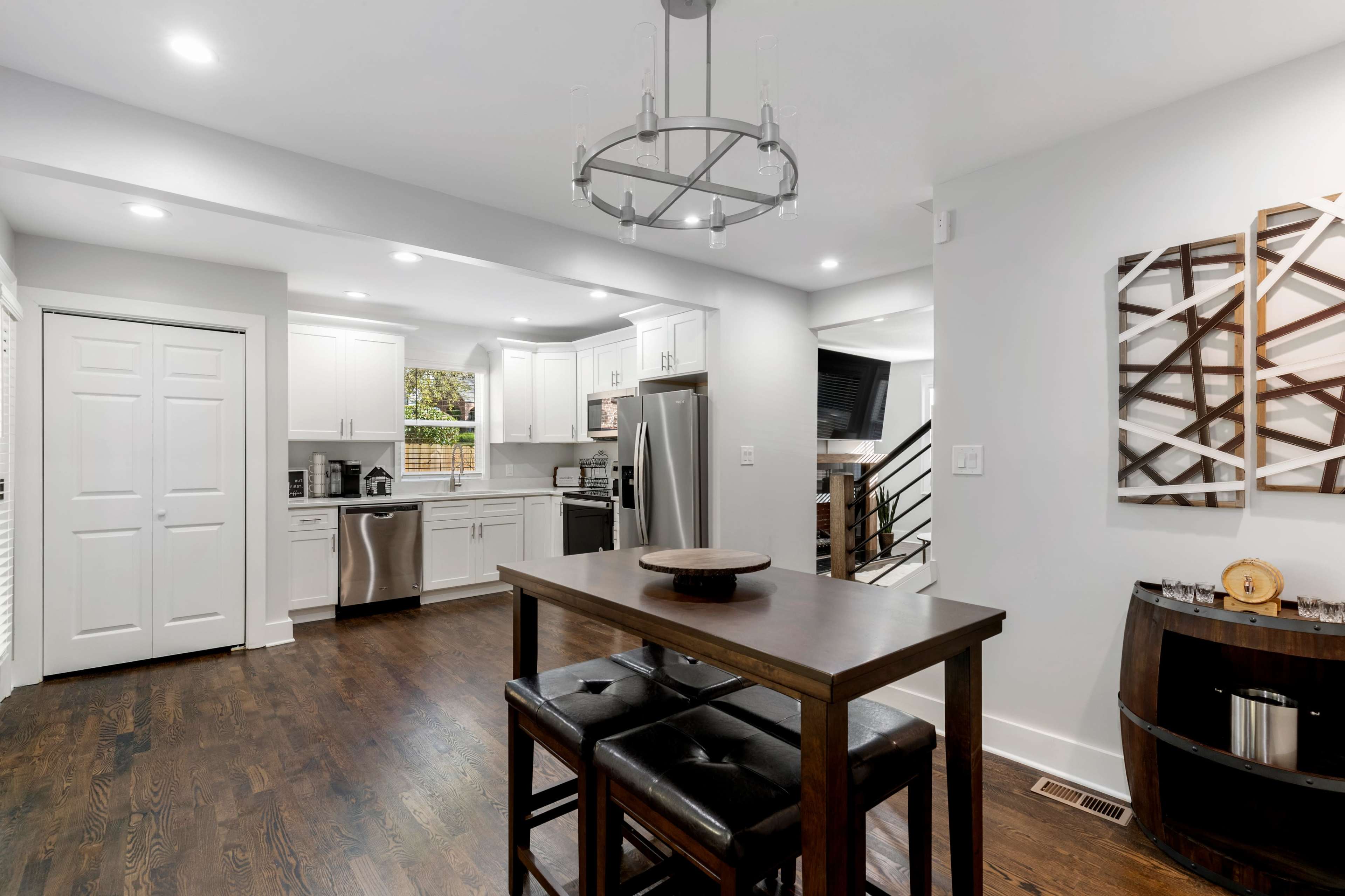 A modern kitchen and dining area with white cabinetry, stainless steel appliances, and dark wooden flooring.