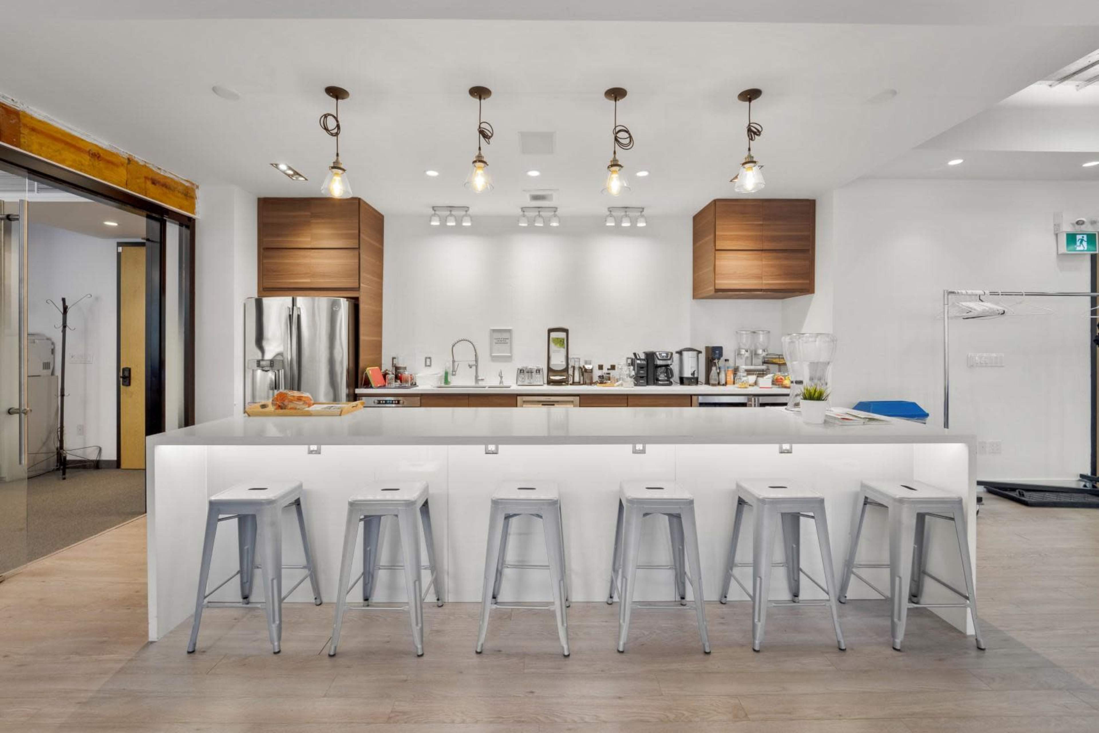 A modern kitchen features a large central island with six metal stools, surrounded by wooden cabinets and various kitchen appliances.