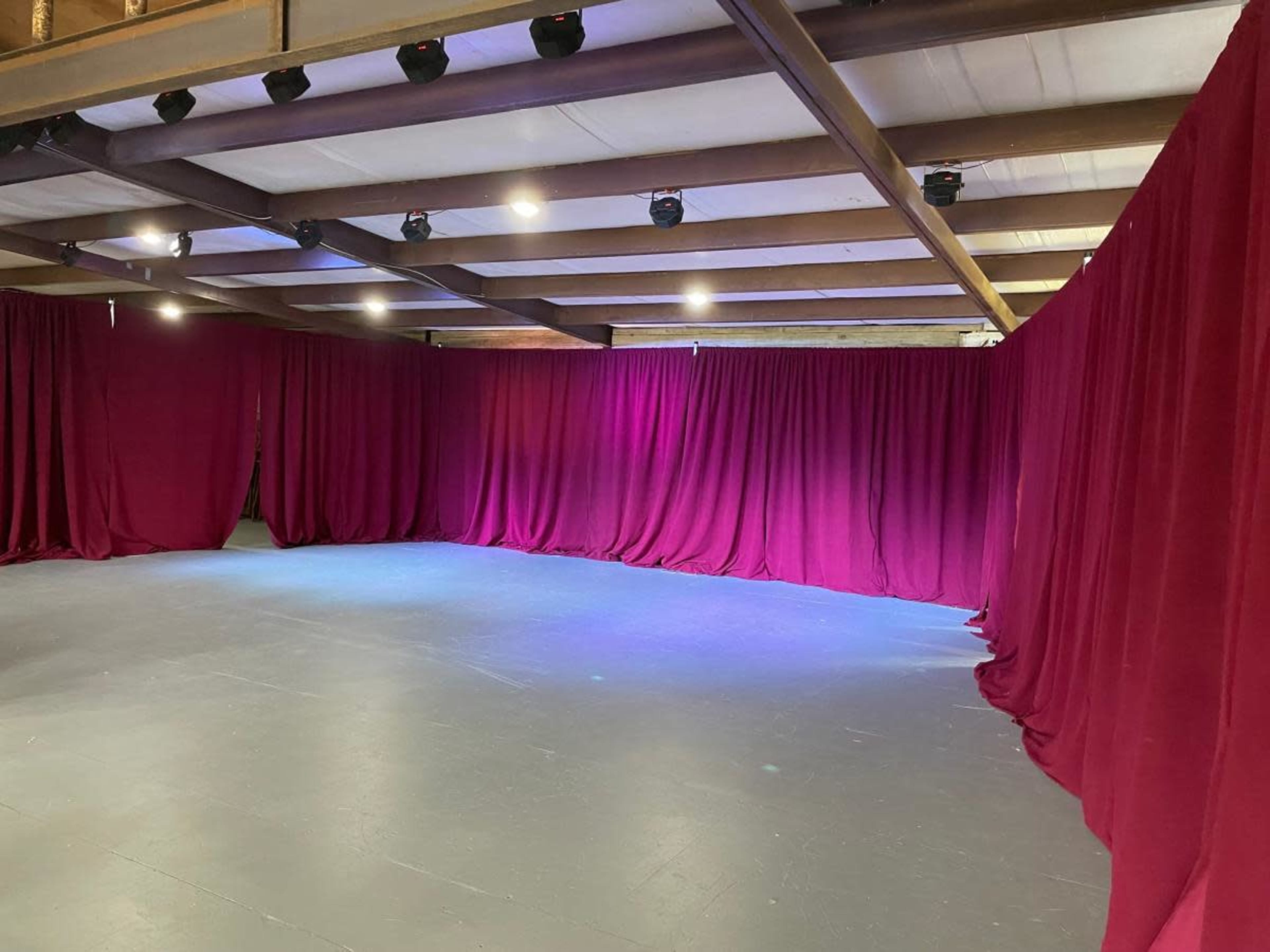 An empty stage area with maroon curtains hanging from the ceiling and soft lighting illuminating the floor.
