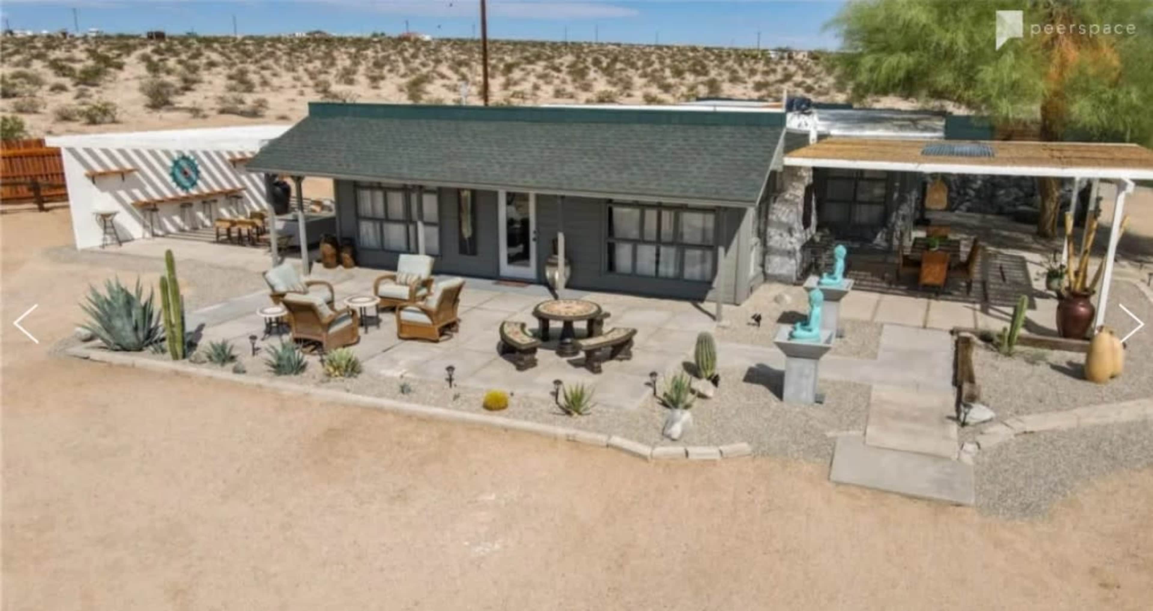 A desert property featuring a single-story house with a porch, surrounded by landscaped gravel and desert plants.