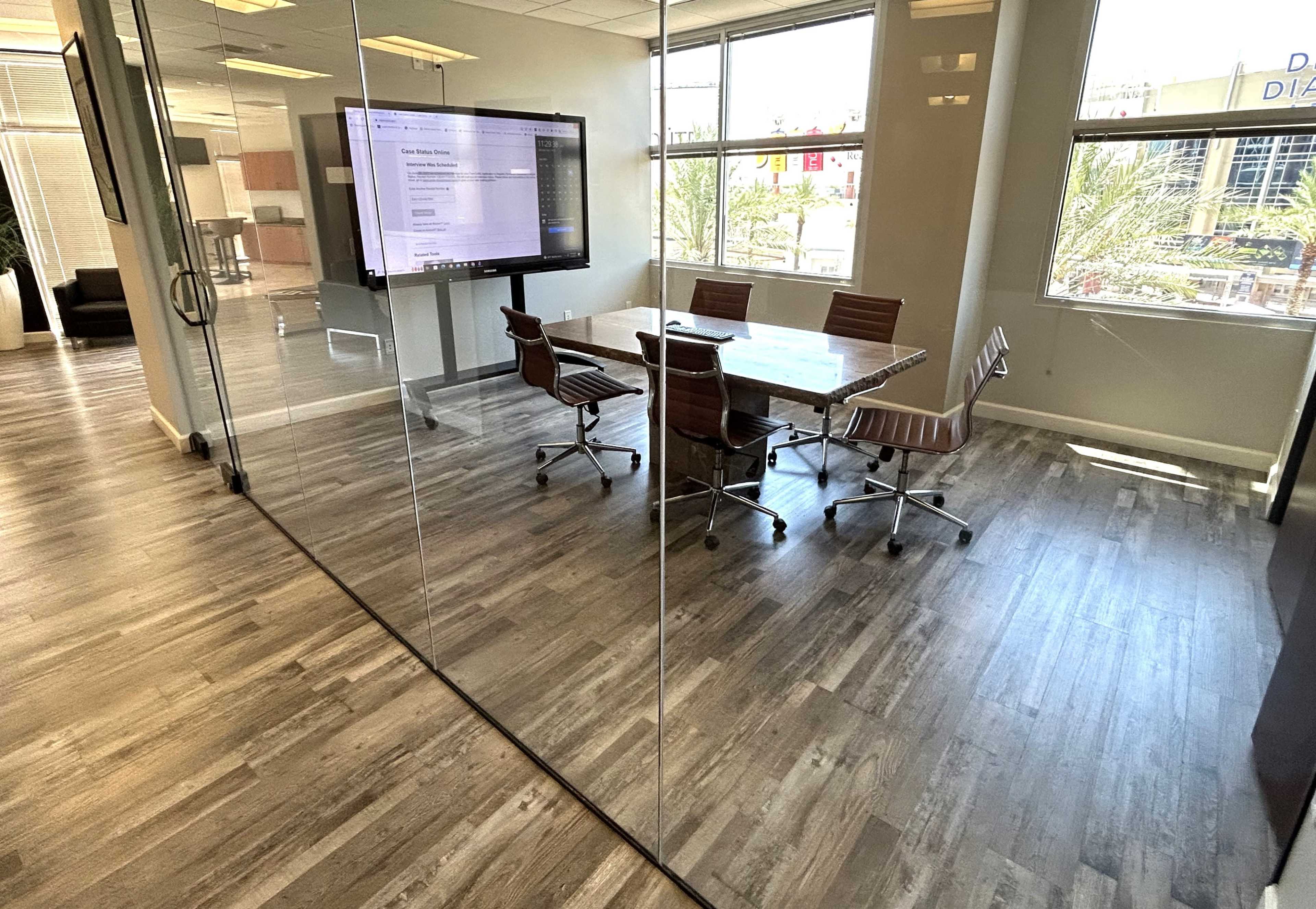A modern conference room with a glass wall, a wooden table, and four brown office chairs.