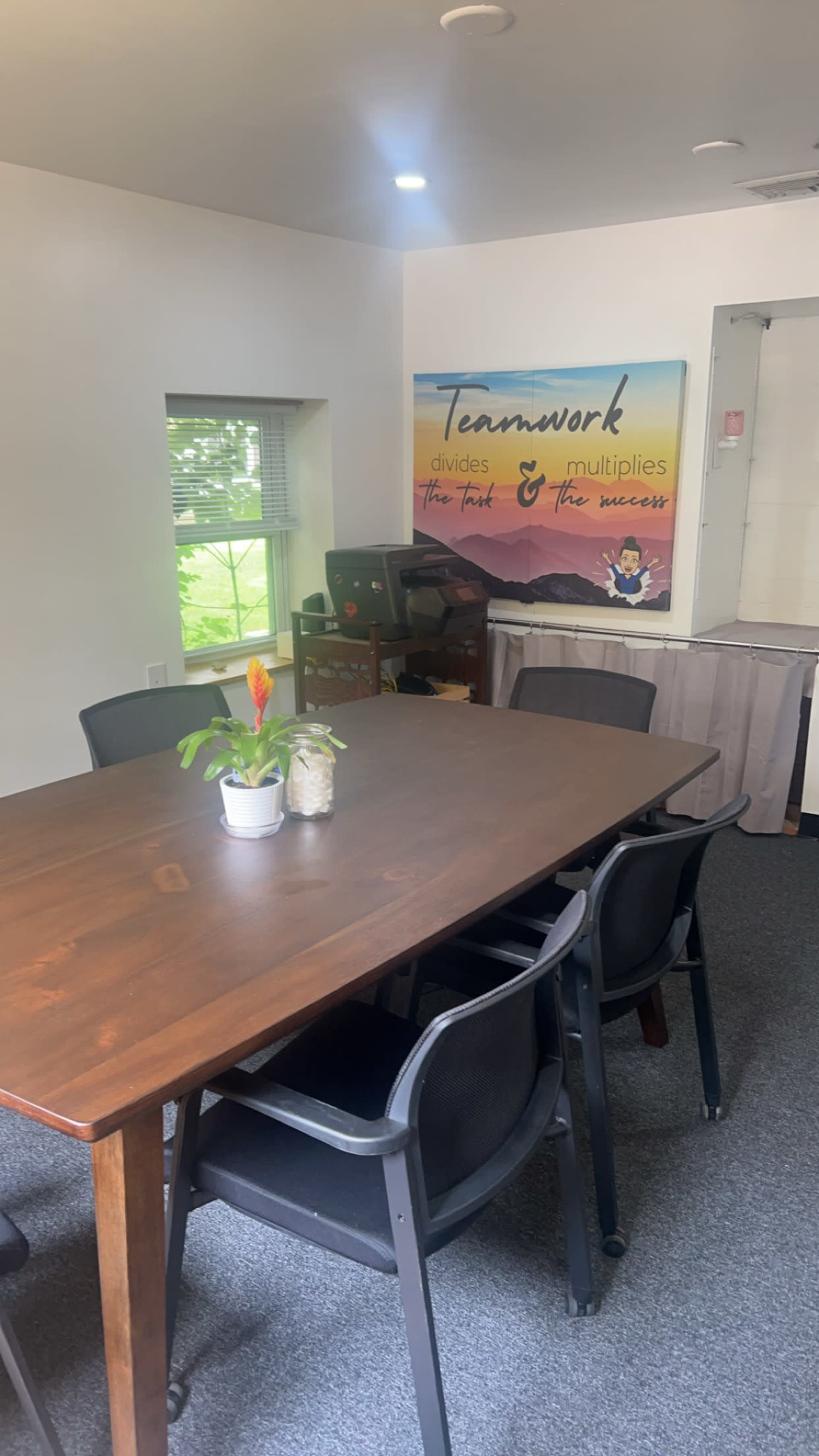 A meeting room featuring a wooden table surrounded by black chairs and a motivational poster on the wall.