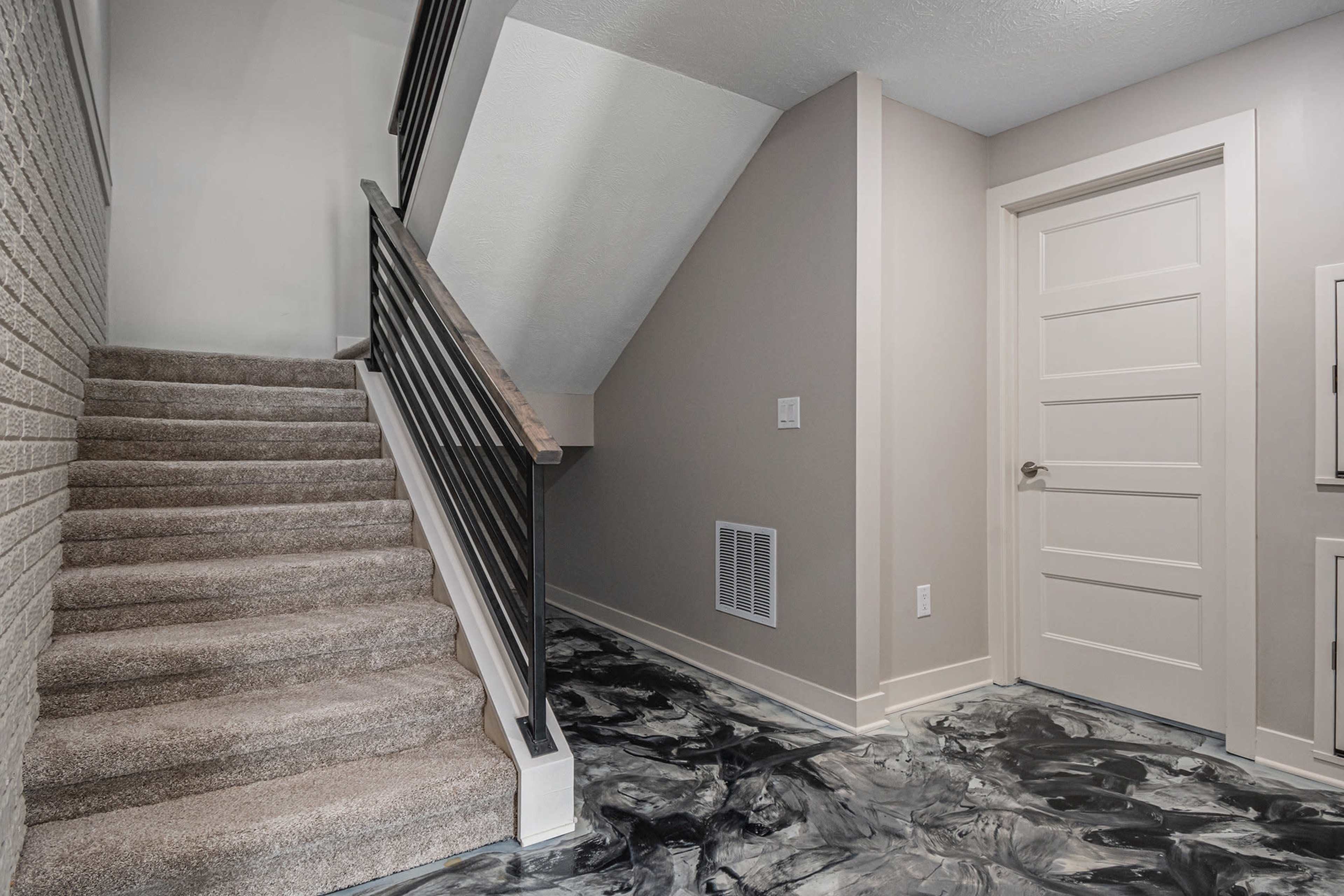 A staircase leads to a landing with a gray wall and a closed door, adjacent to a floor with a black and gray marbled finish.