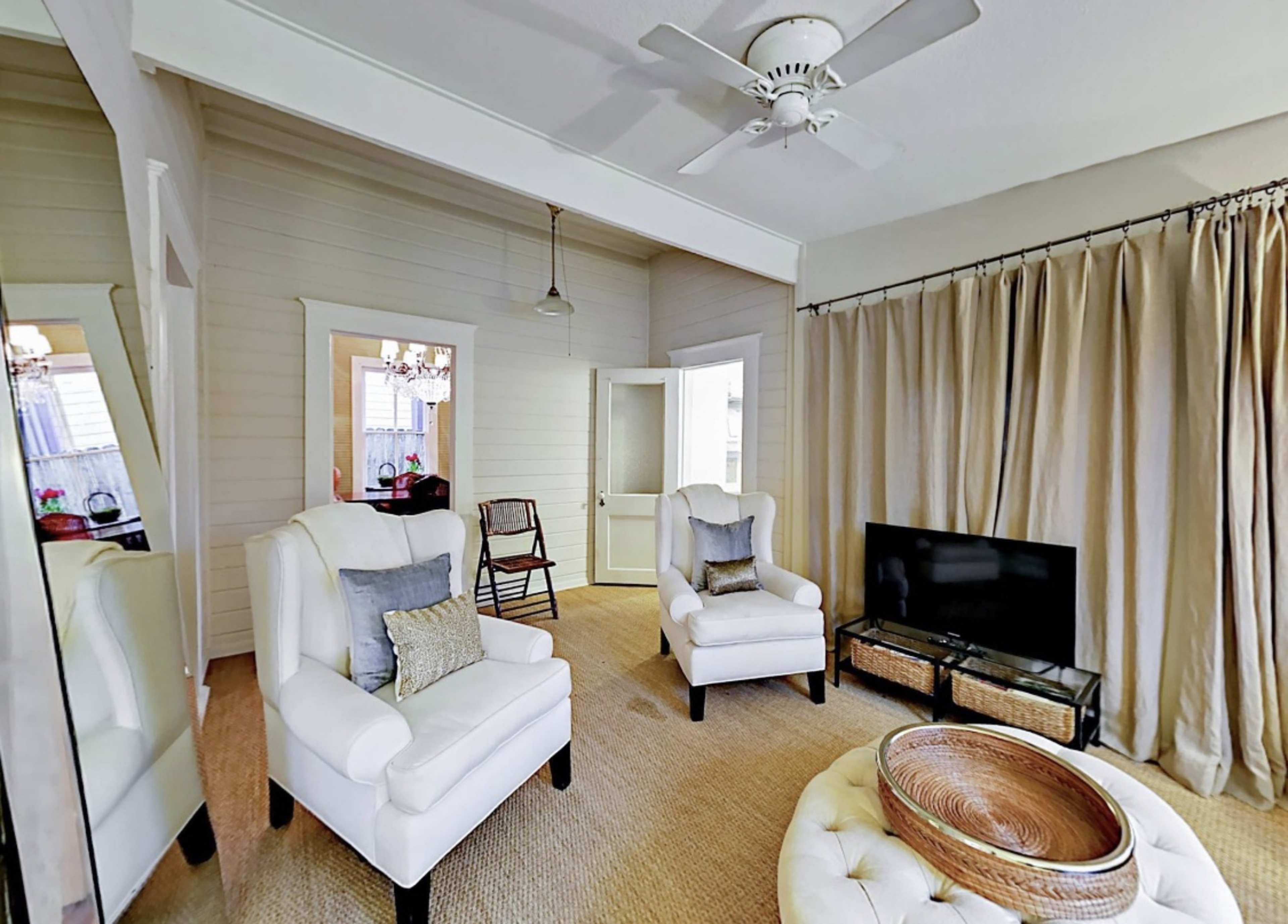 The living room features two white armchairs, a round coffee table, a television, and a doorway draped with curtains.