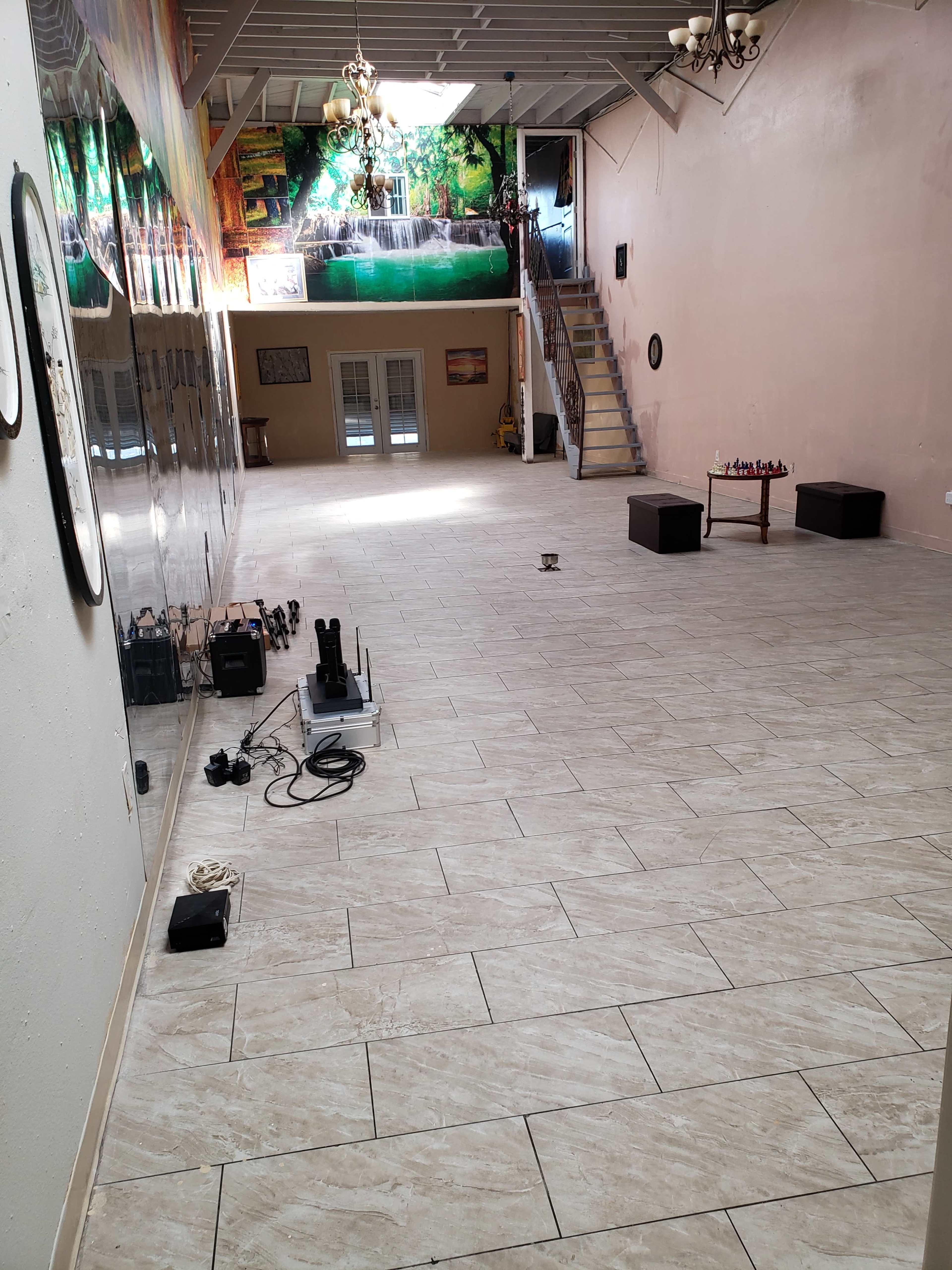 The image shows a spacious, empty room with tiled flooring, large mirrors on one wall, and a staircase leading to an upper area.