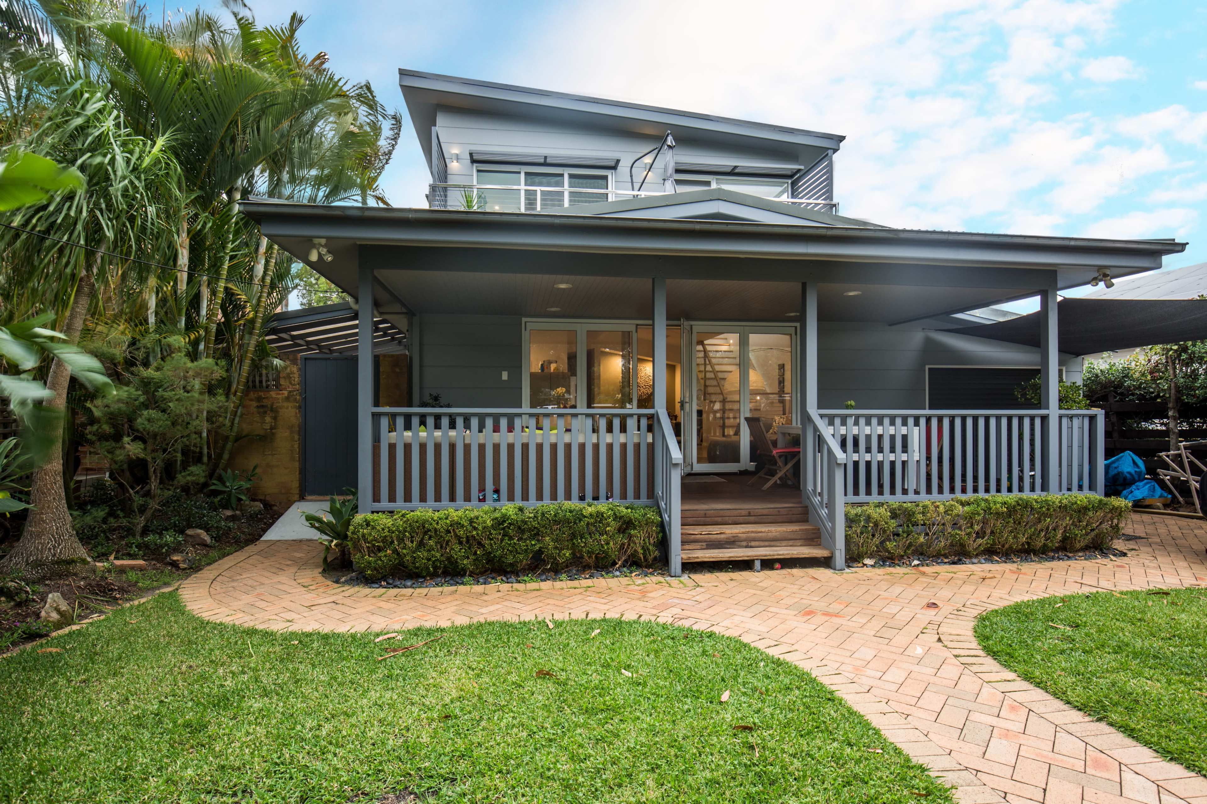 A two-story gray house with a front porch, surrounded by neatly landscaped gardens and a brick pathway.