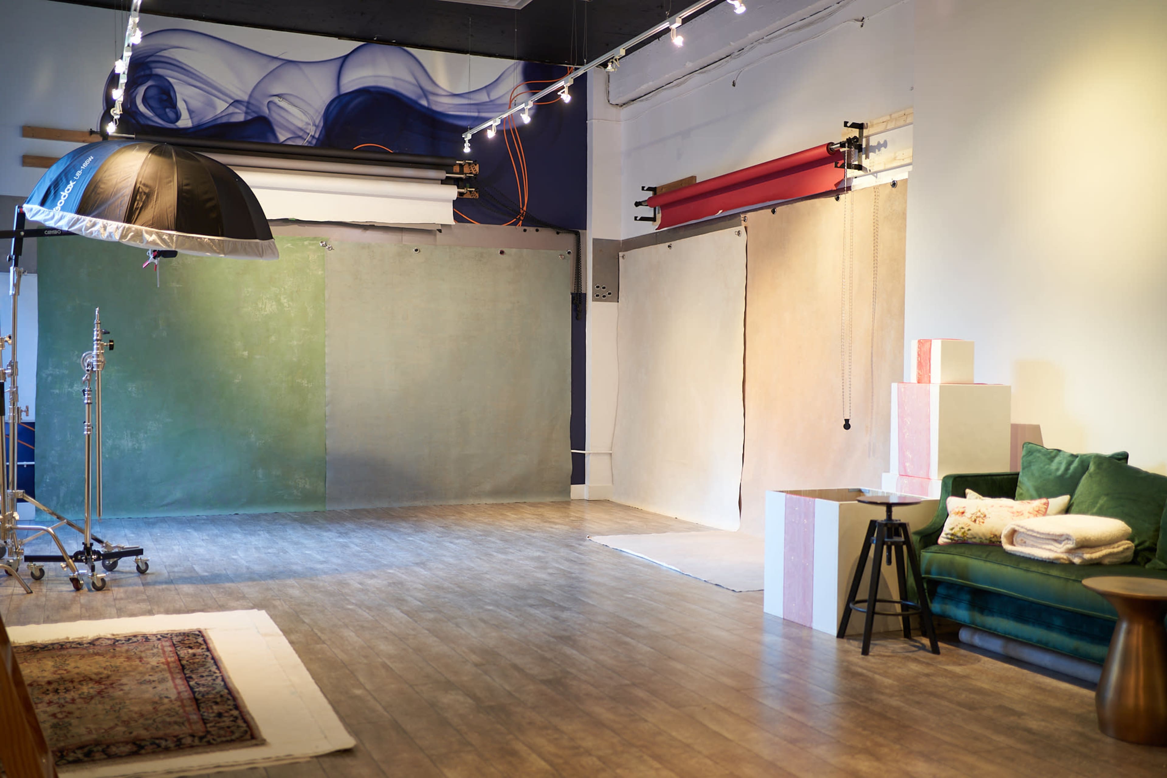 The image shows a photography studio with various backdrop options, a green velvet couch, and soft lighting.