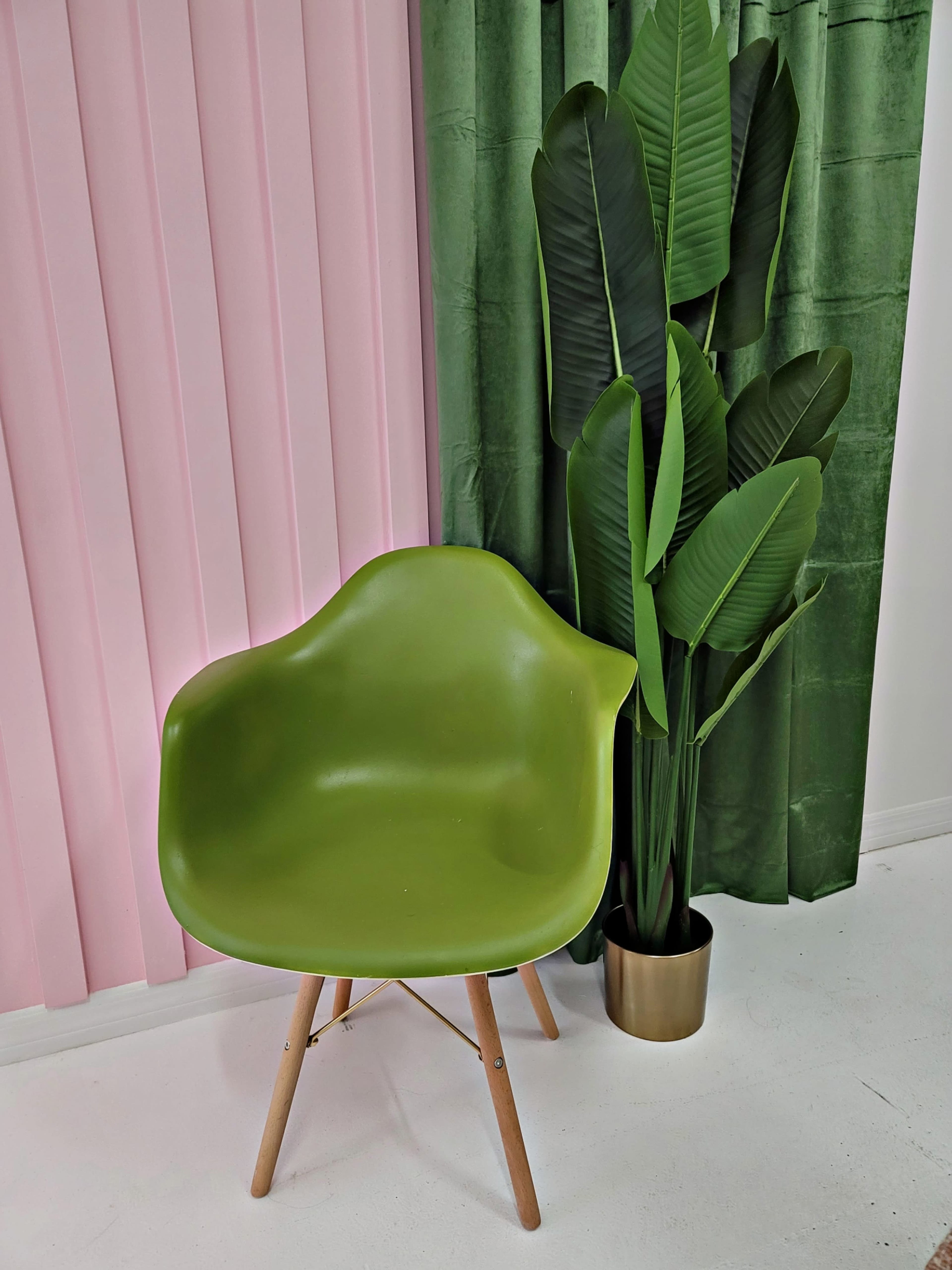 A green chair sits next to a potted plant, against a backdrop of pink and green curtains.