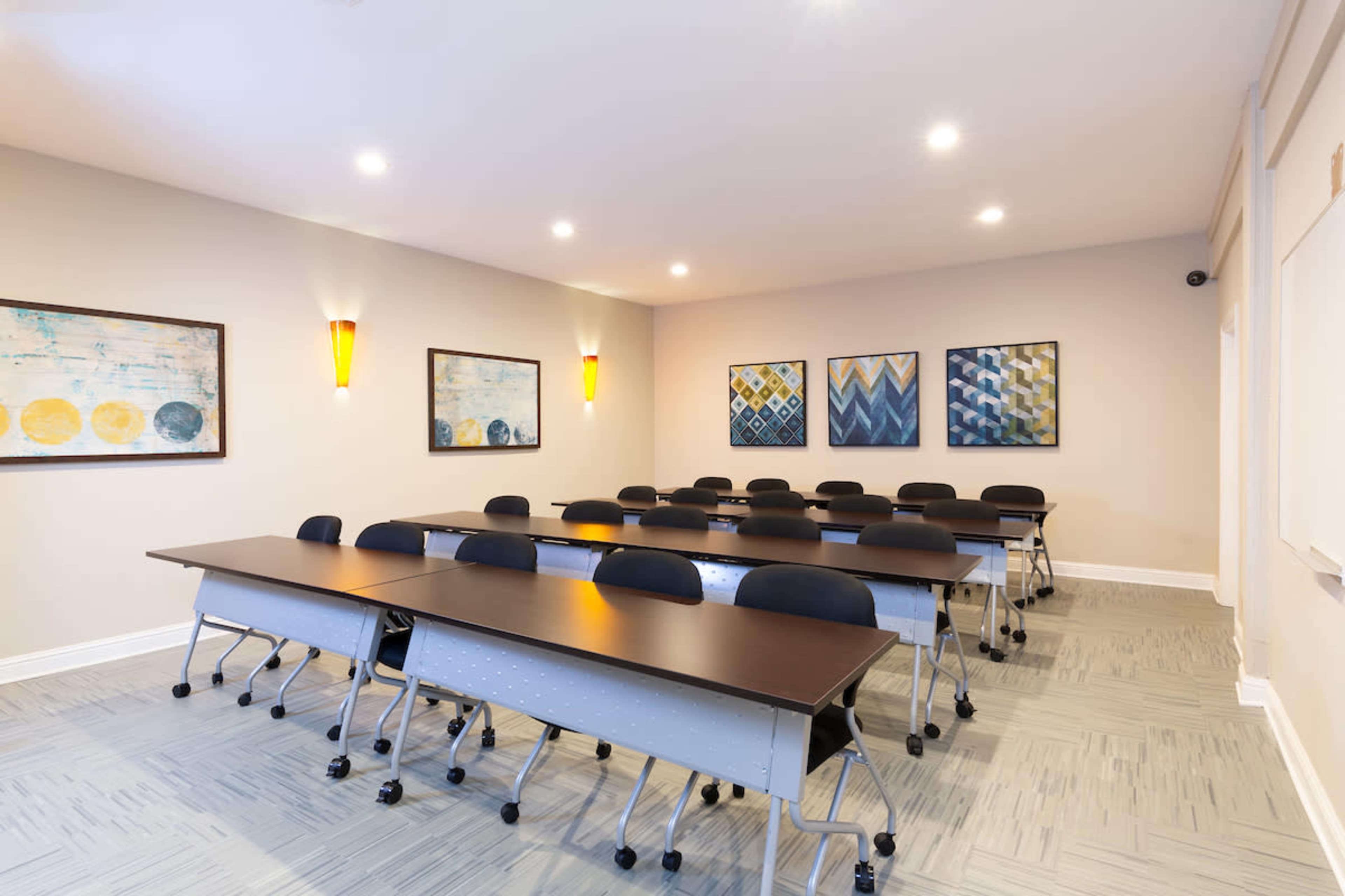 A spacious conference room arranged with multiple rows of black chairs and long tables, featuring decorative art on the walls.