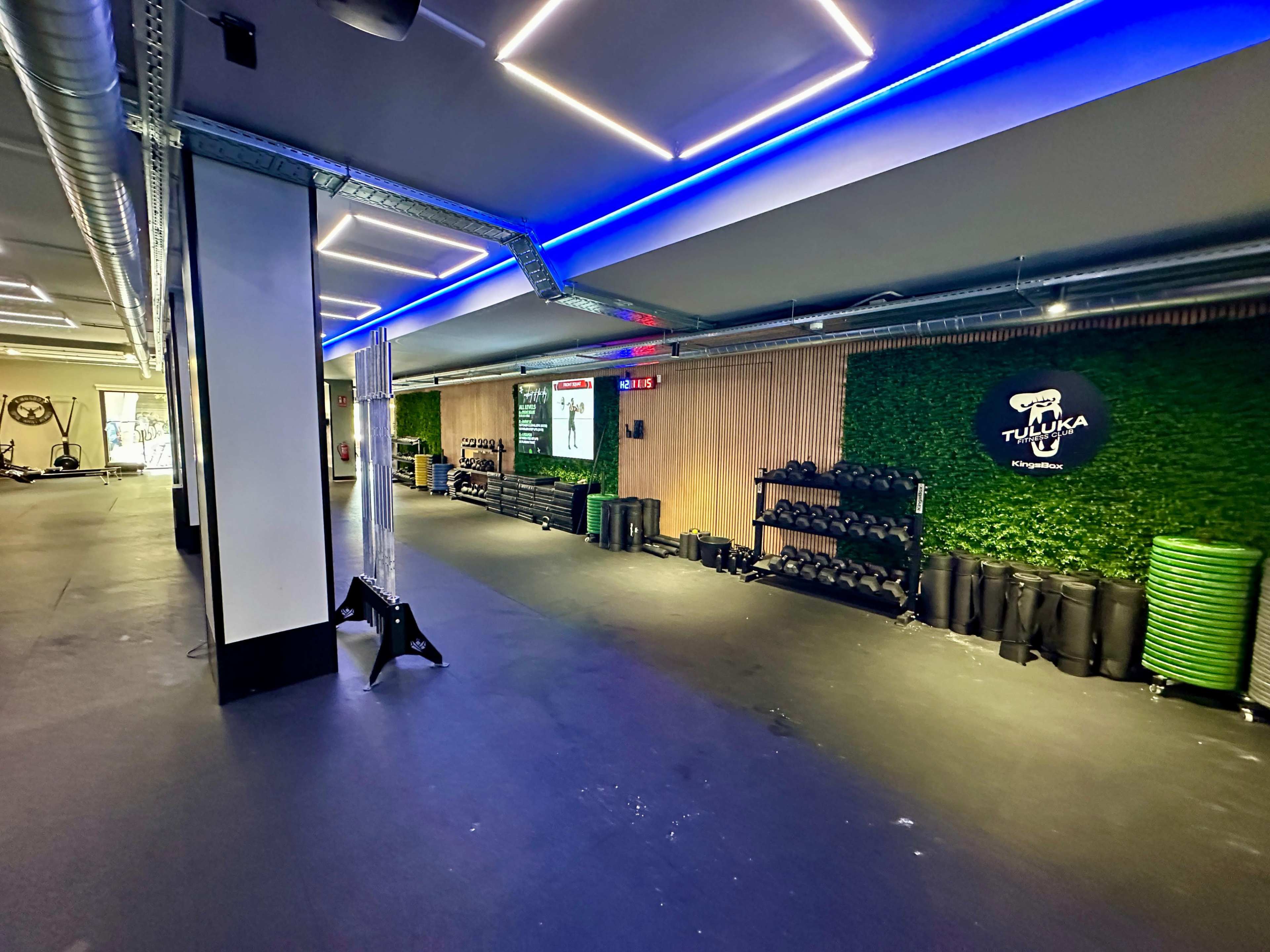 A spacious gym interior with exercise equipment, including dumbbells and mats, illuminated by blue LED lights.
