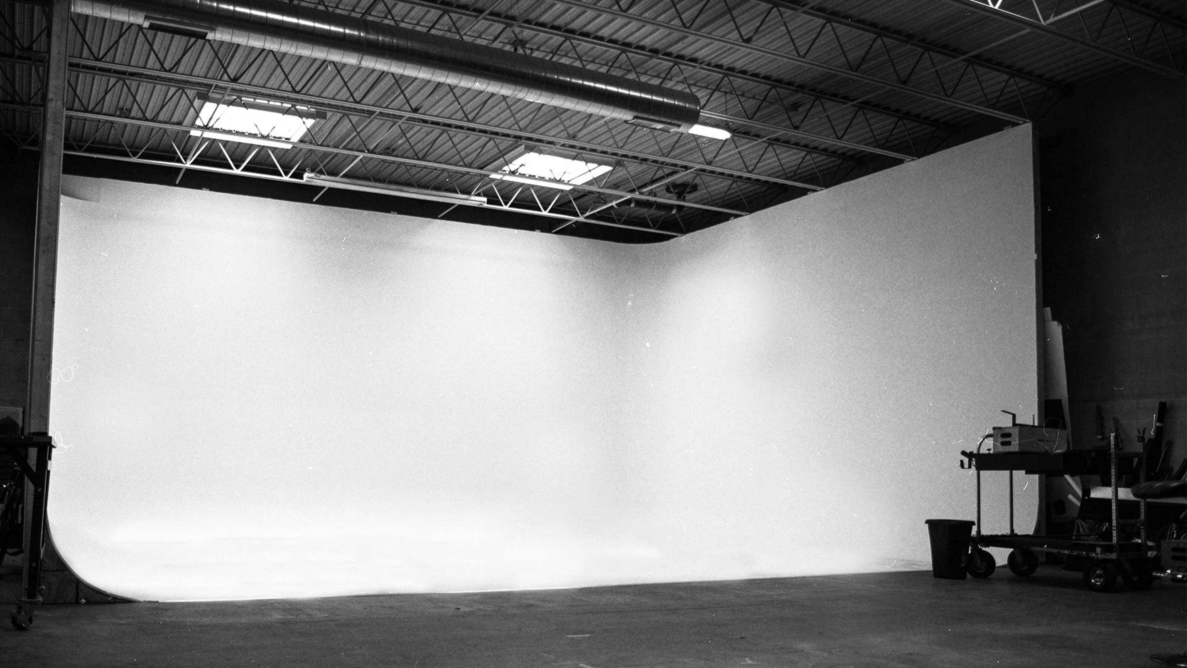 The image depicts a spacious, empty studio with white walls and a seamless backdrop.
