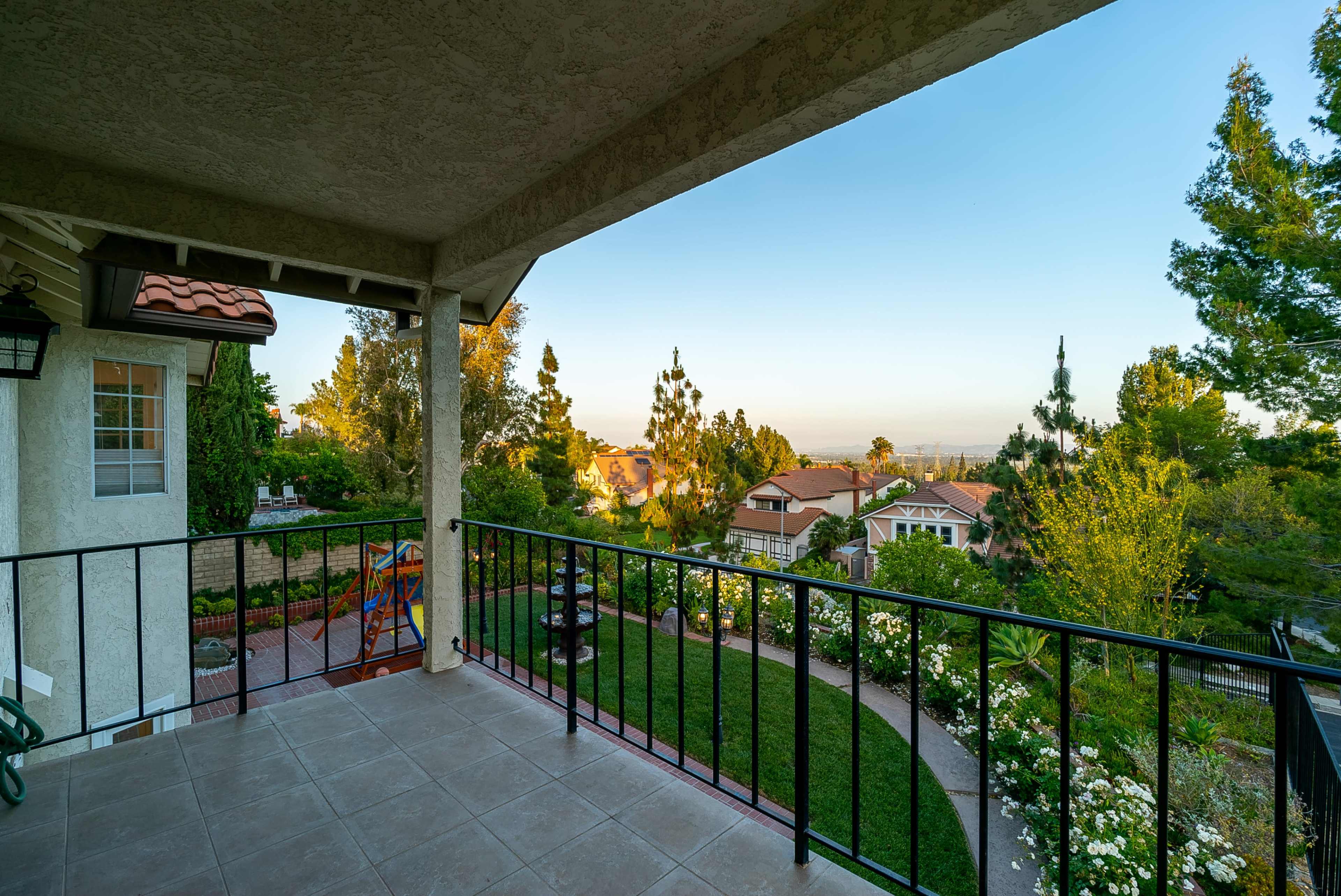 A balcony overlooking a landscaped yard with houses and trees in the distance.