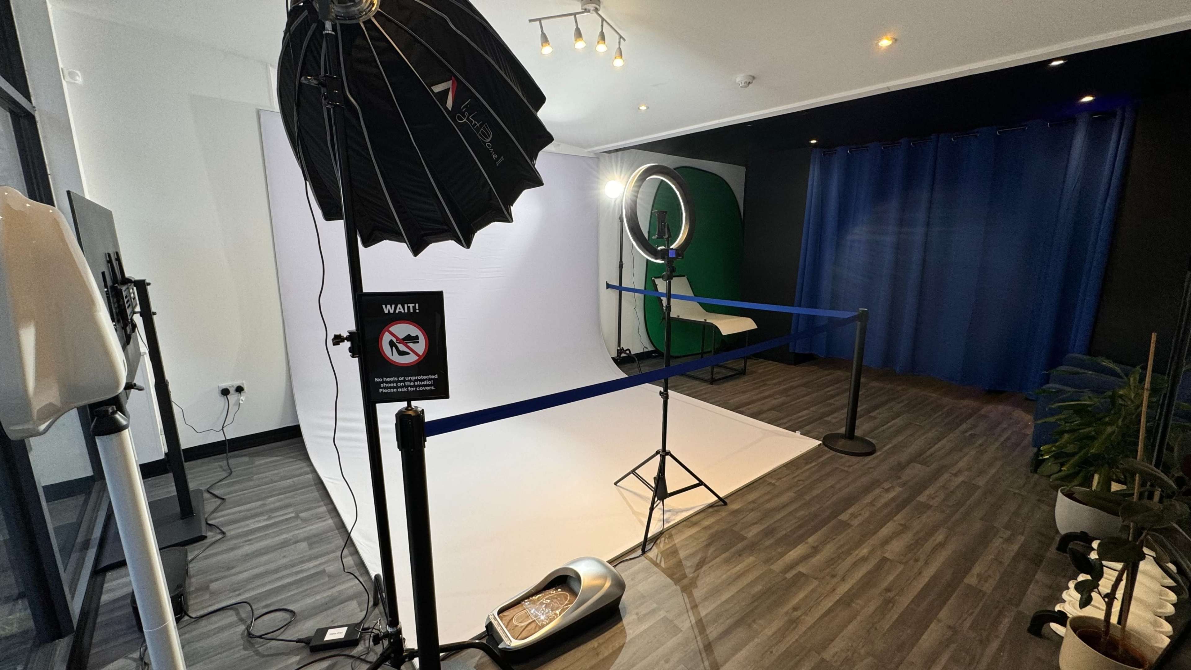 A photo studio setup with a white backdrop, ring light, softbox, and a blue curtain in the background.