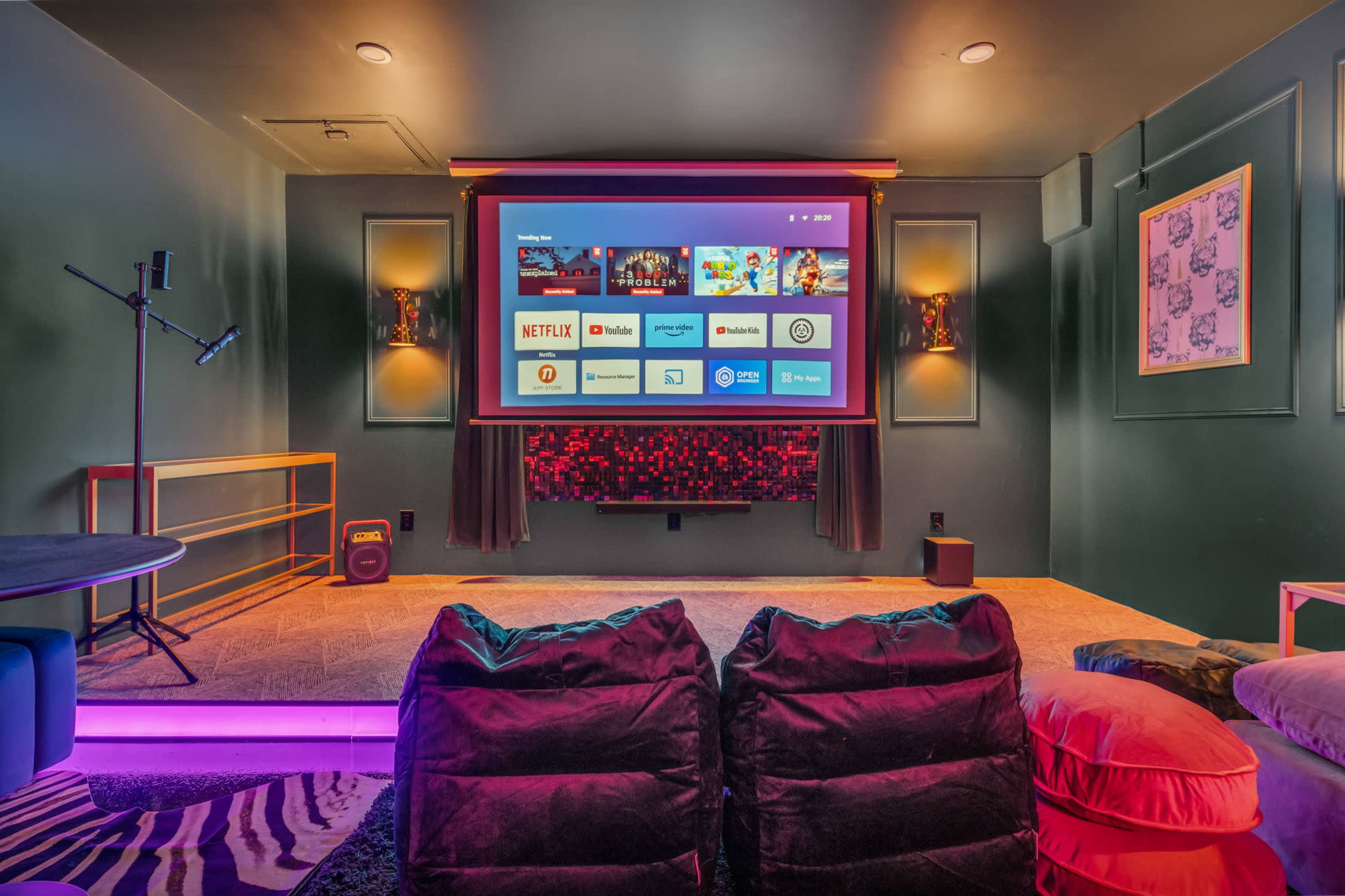 The image shows a home theater setup featuring a large projection screen, a cozy seating area with plush bean bags, and a darkly painted room.