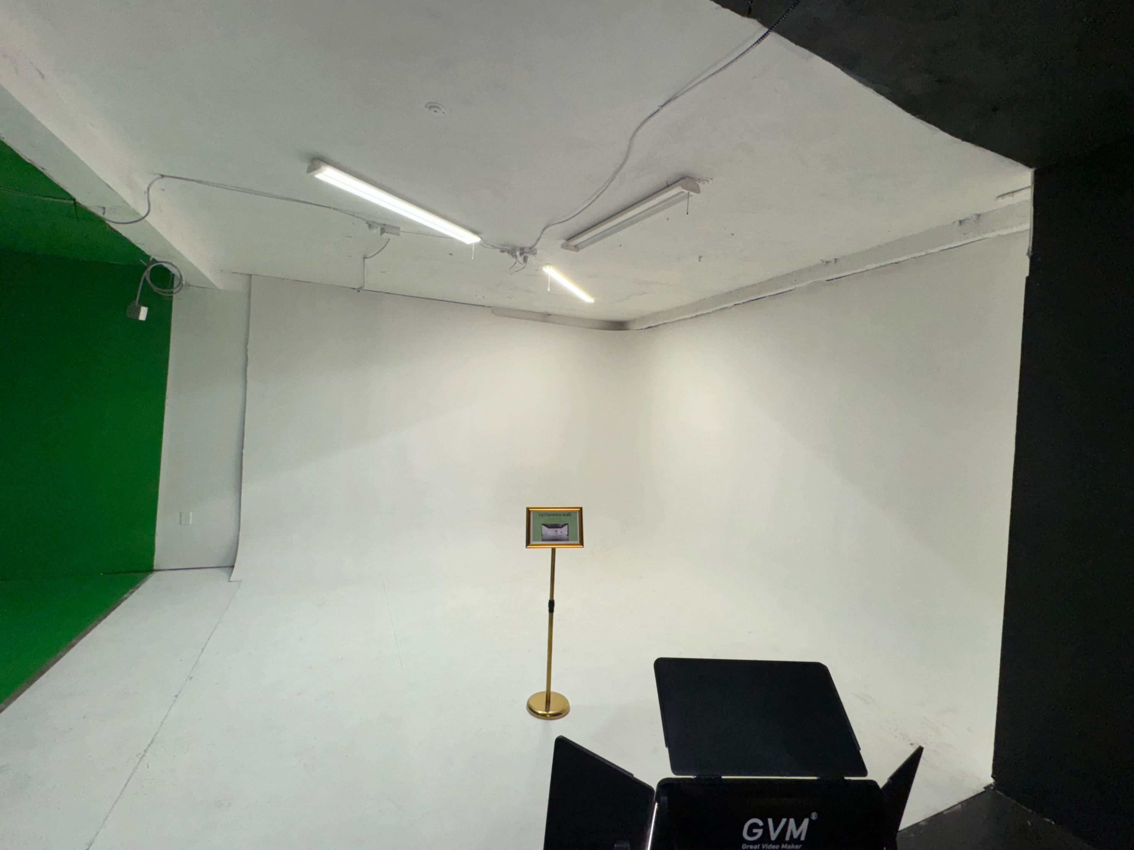 The image shows a spacious studio with a green wall on one side, a white wall on the opposite side, and a stand holding a display in the center.