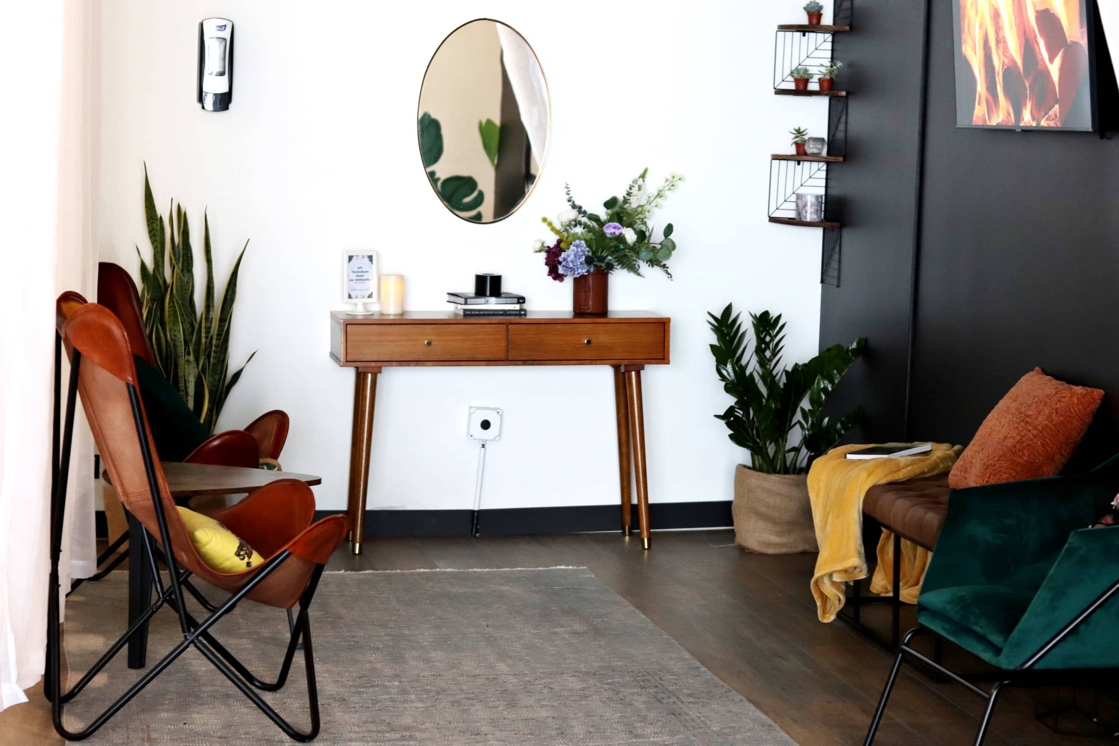 A cozy living area features a wooden console table, a mirror, various plants, and comfortable seating in a blend of colors.