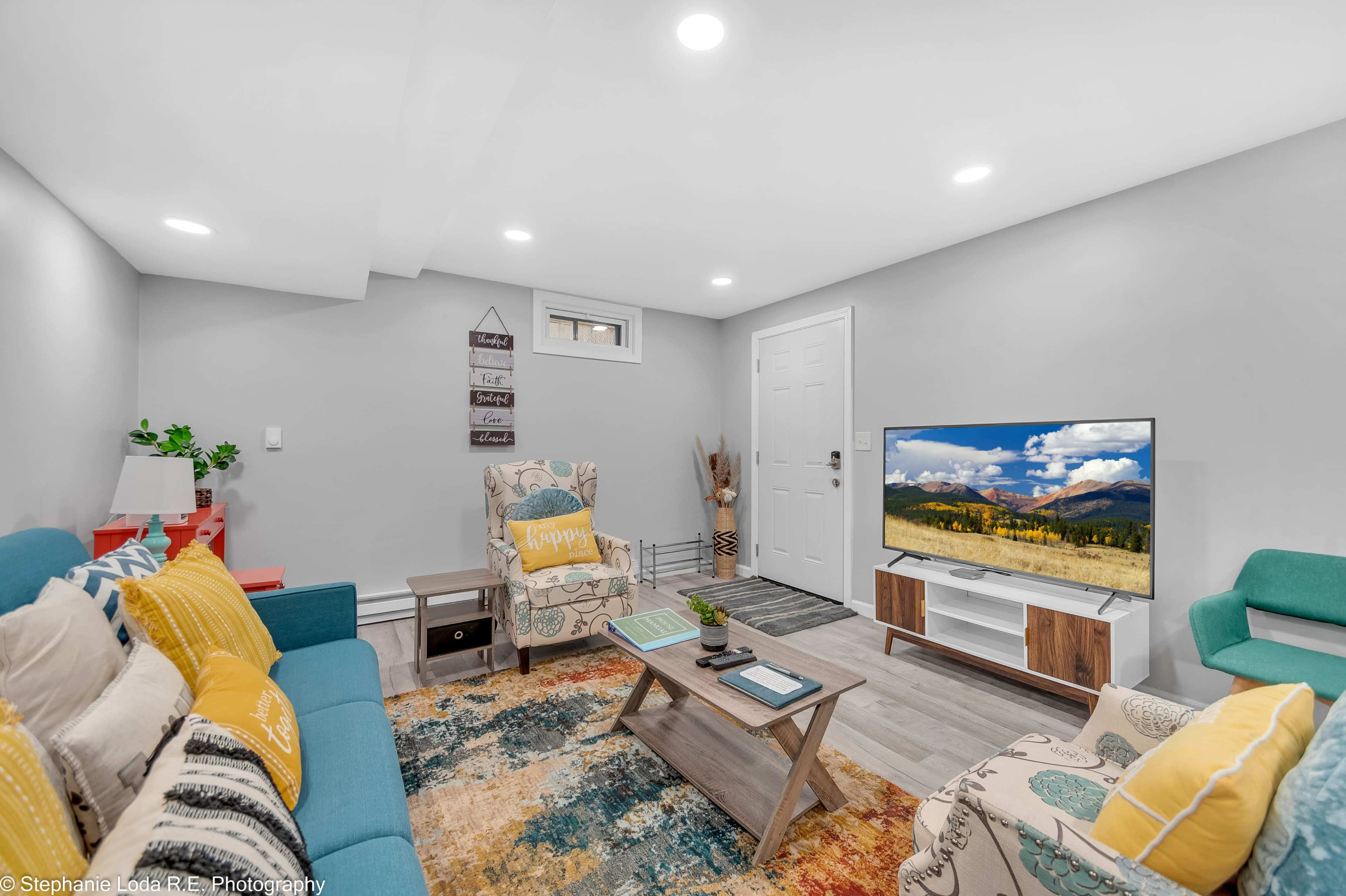 The room features a cozy seating area with colorful chairs, a coffee table, and a television against a light gray wall.