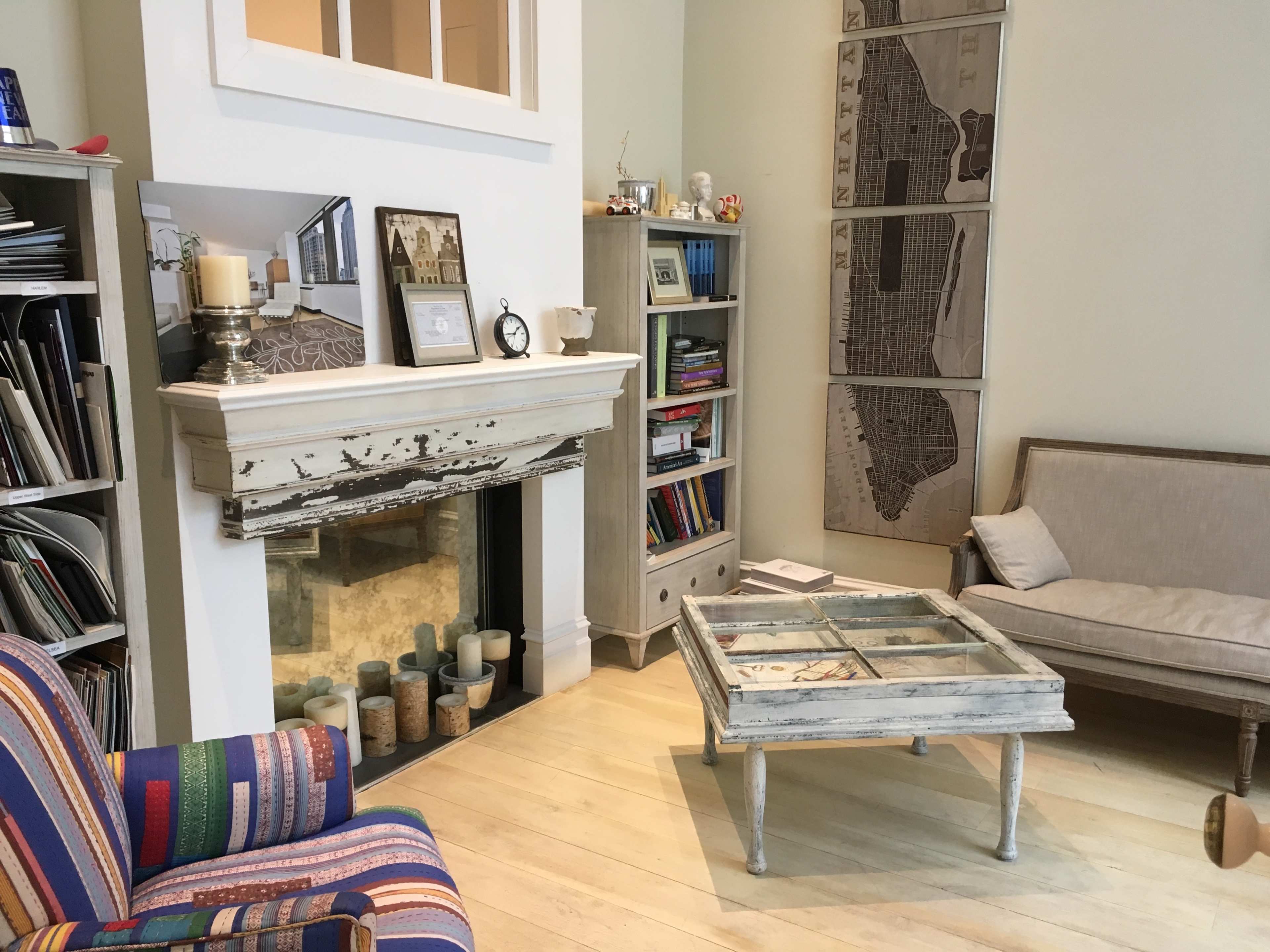 A living room with a striped armchair, a glass-top coffee table, a bookshelf filled with books, and a fireplace surrounded by candles.