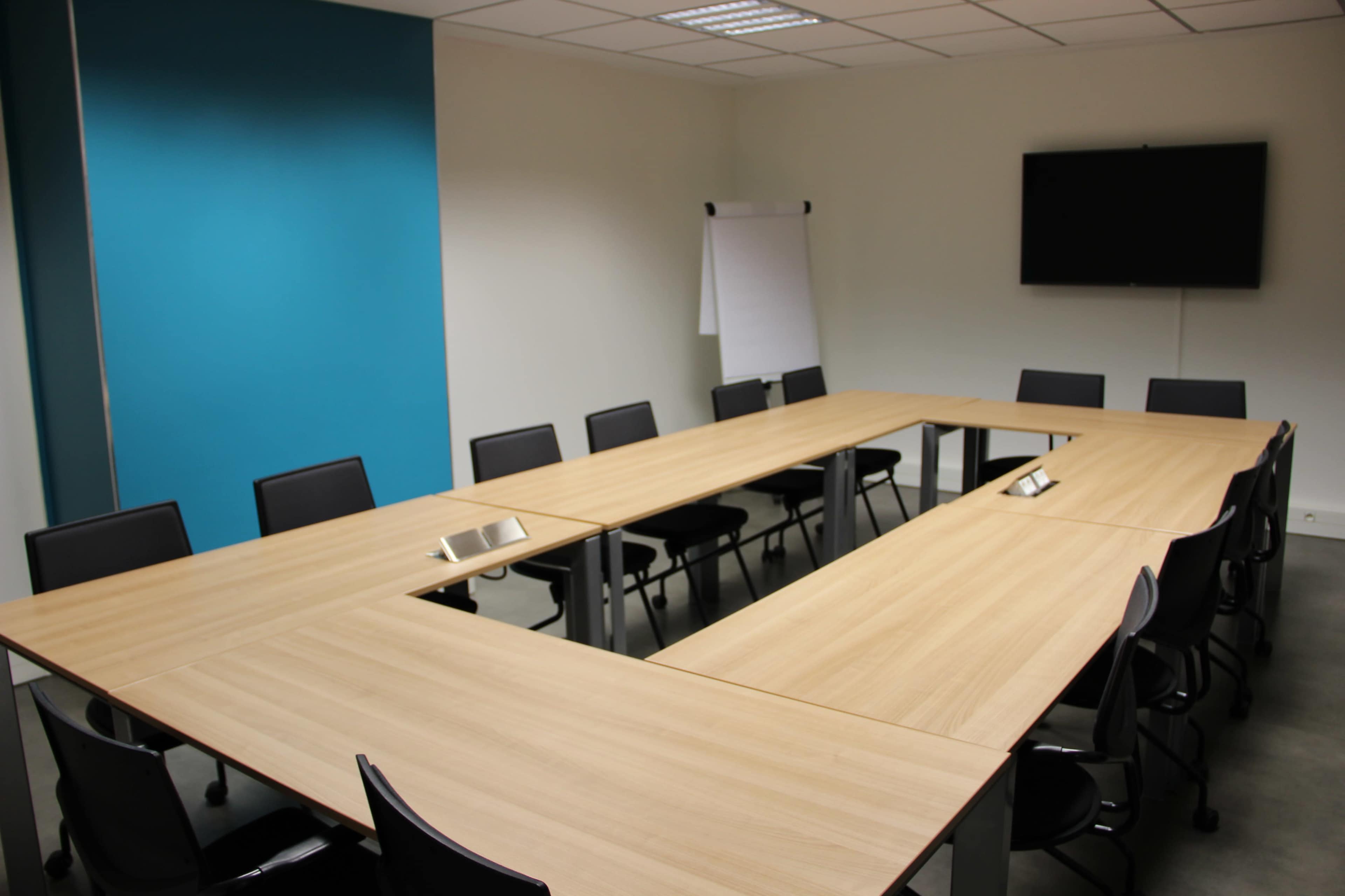 A large conference room features a rectangular table surrounded by chairs, with a presentation screen and a flip chart against the walls.