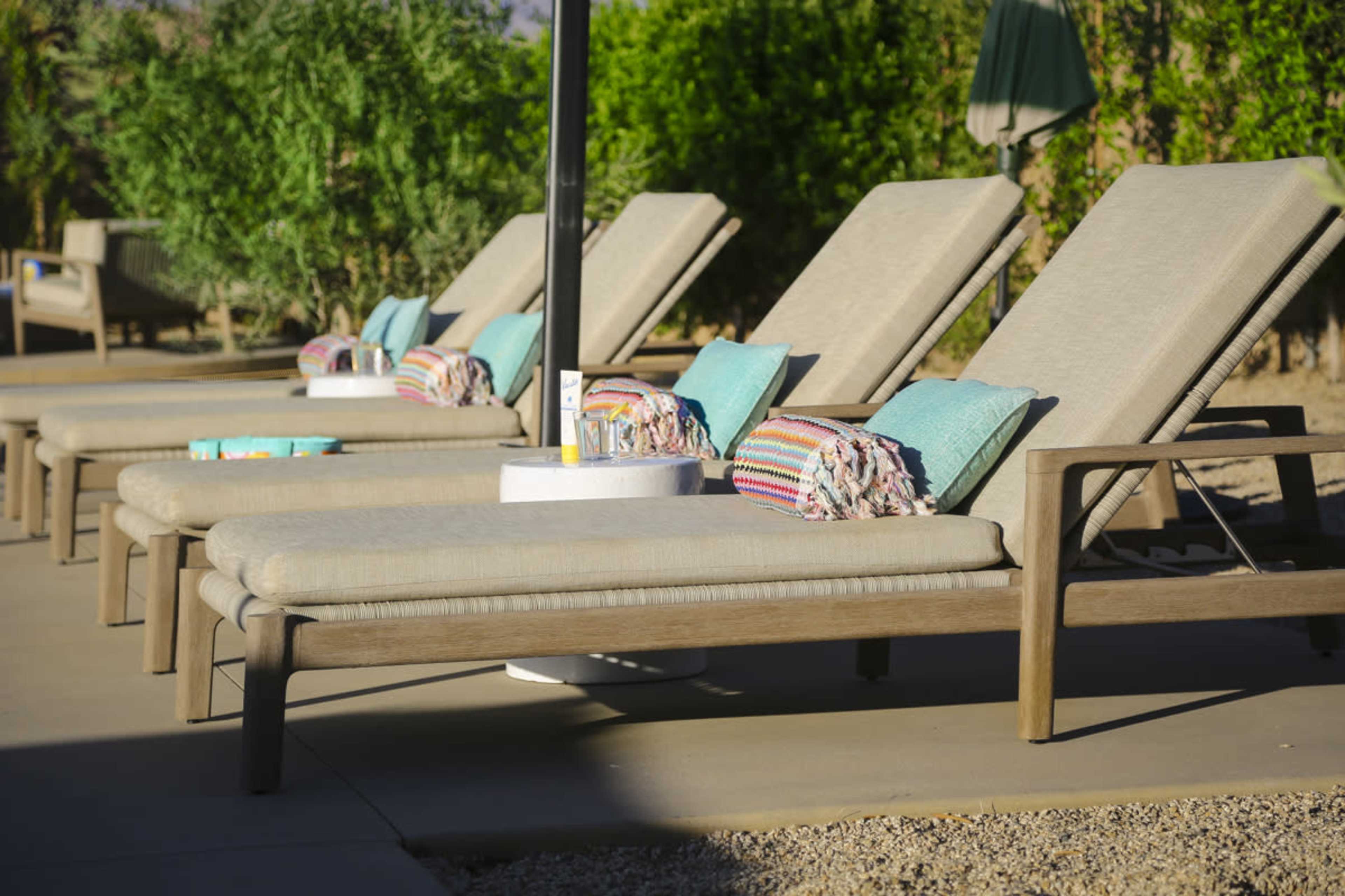 Several lounge chairs with colorful towels and cushions are arranged by a poolside area surrounded by greenery.