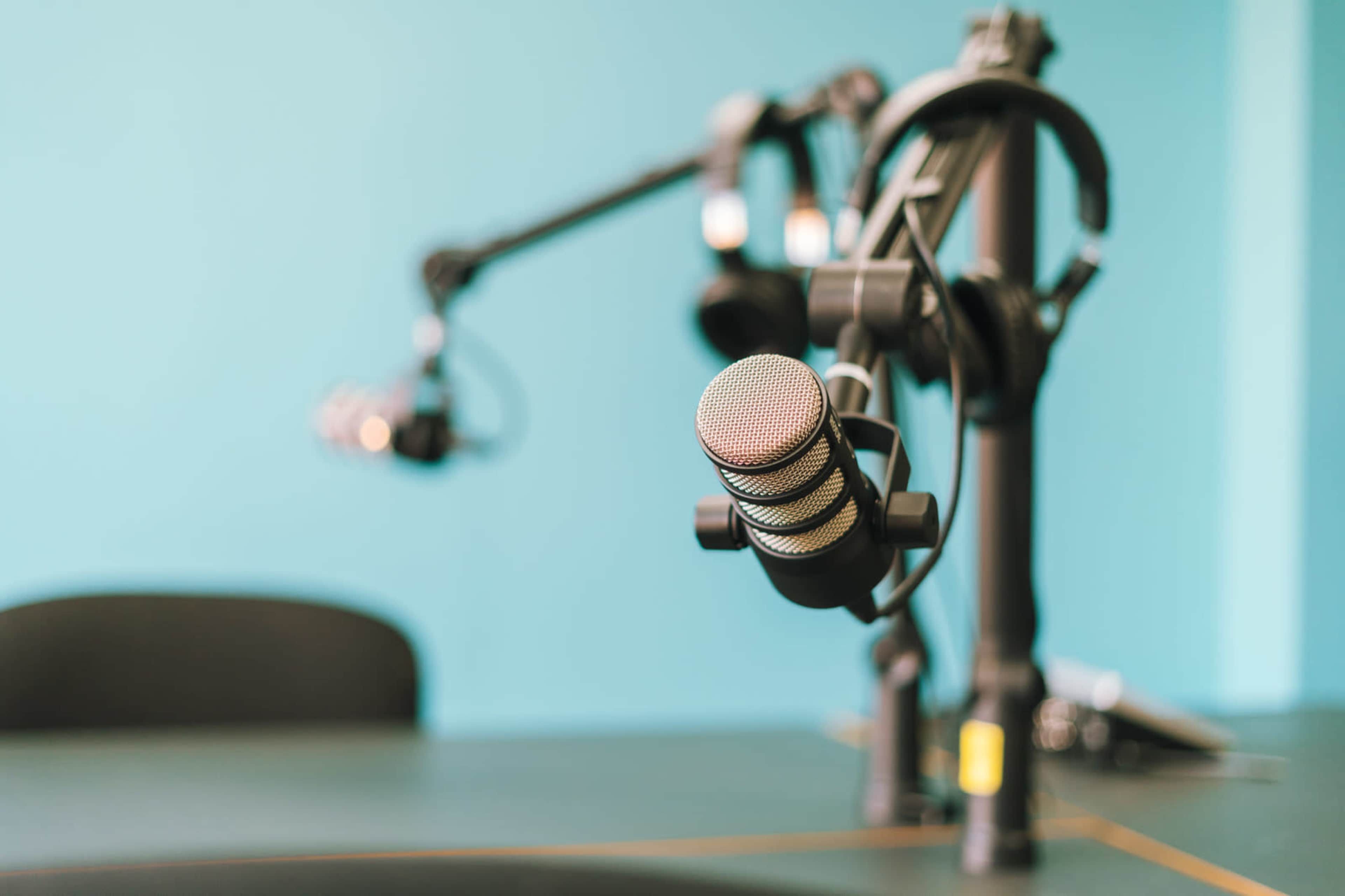 A close-up of a microphone on a stand in a studio with a turquoise wall in the background.