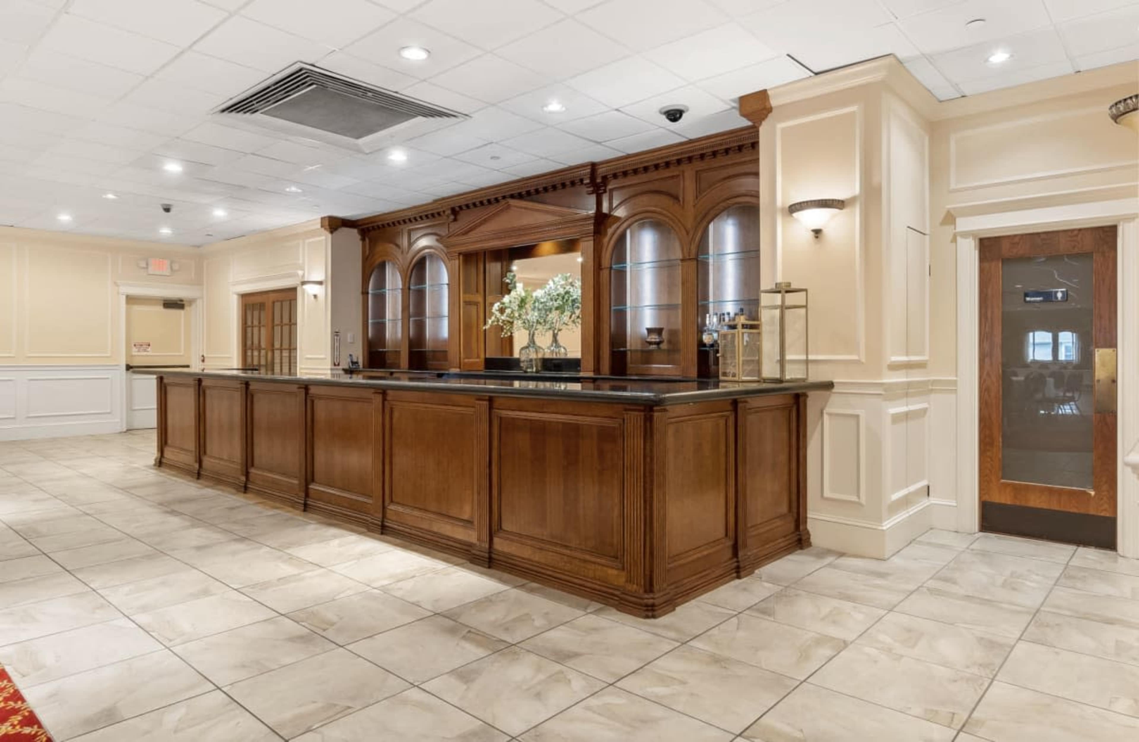 The image shows a hotel lobby reception area with a wooden front desk and a tile floor.