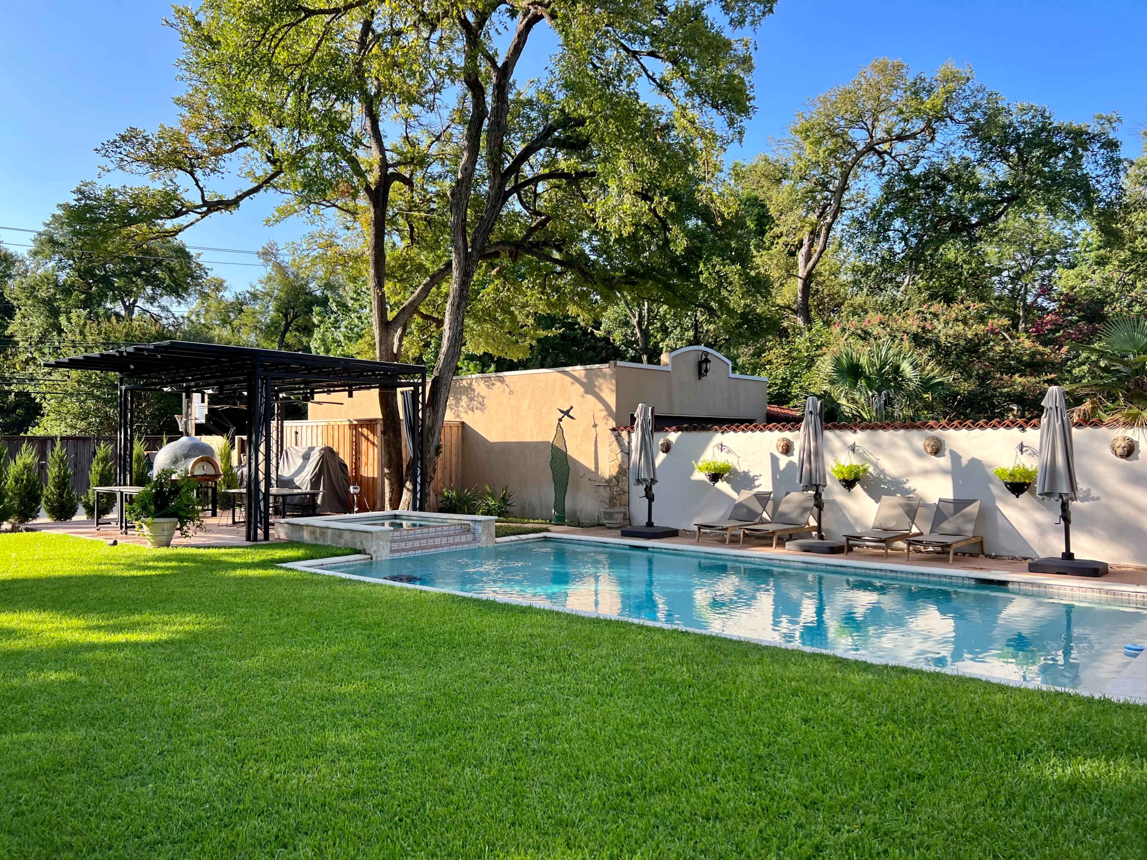 A landscaped backyard featuring a swimming pool surrounded by lounge chairs and a pergola.