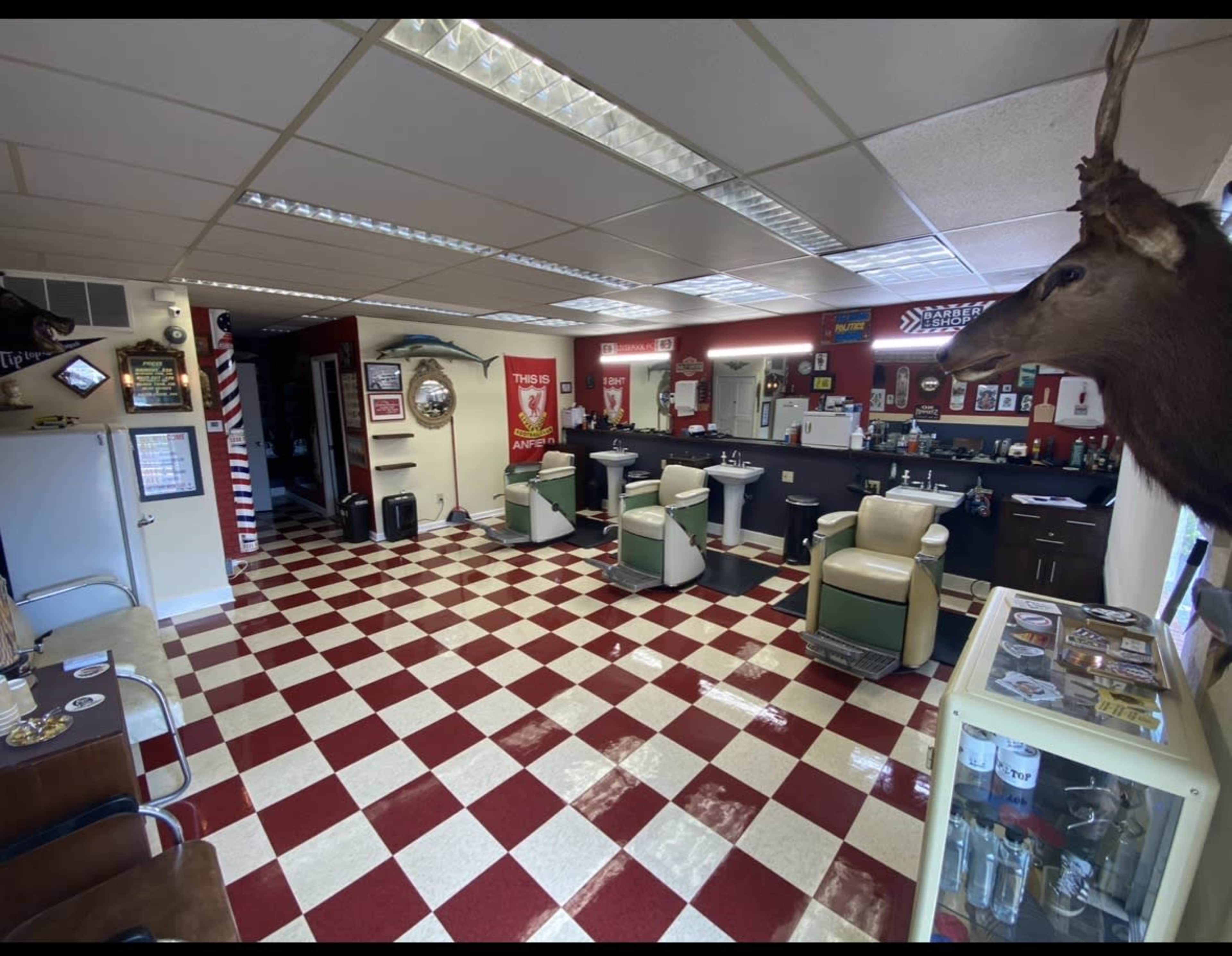 The image shows a retro-style barbershop featuring red and white checkered floors, several barber chairs, and various decorations on the walls.