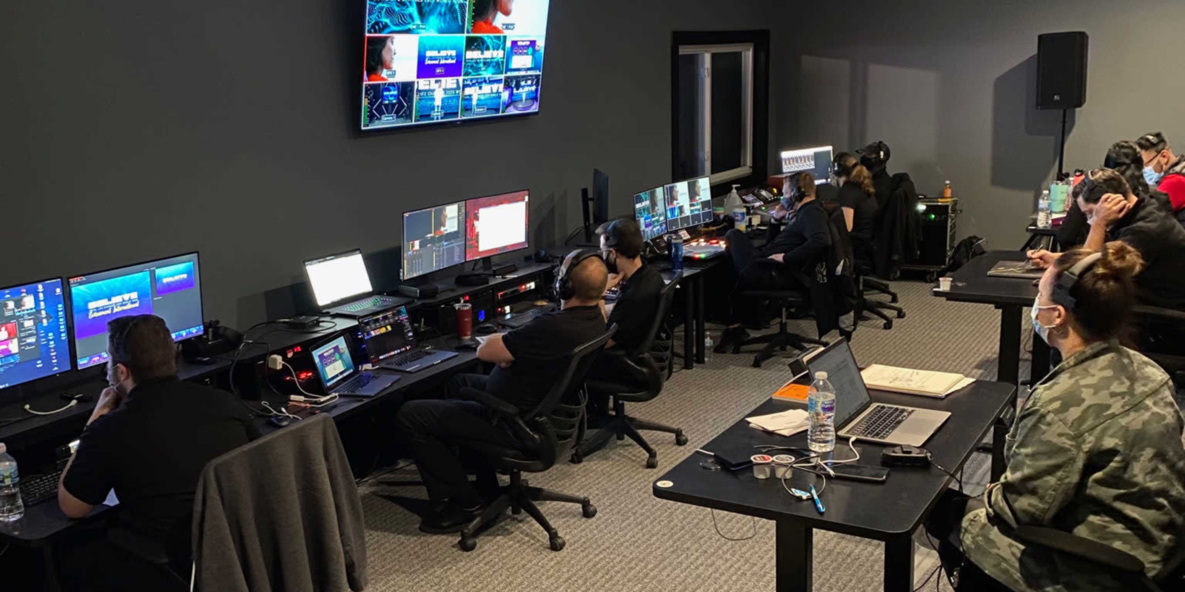 A team of individuals works at computer stations in a dark room filled with multiple monitors and digital equipment.