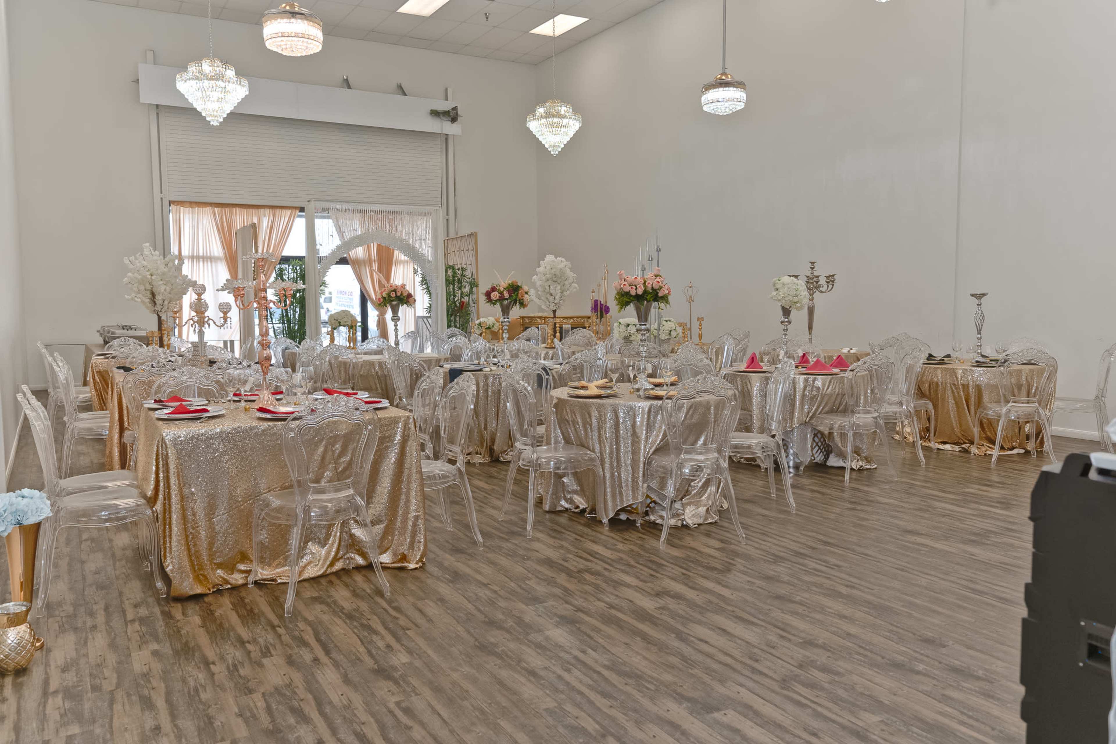 The image shows a banquet hall set up with multiple tables covered in gold tablecloths and adorned with floral centerpieces.