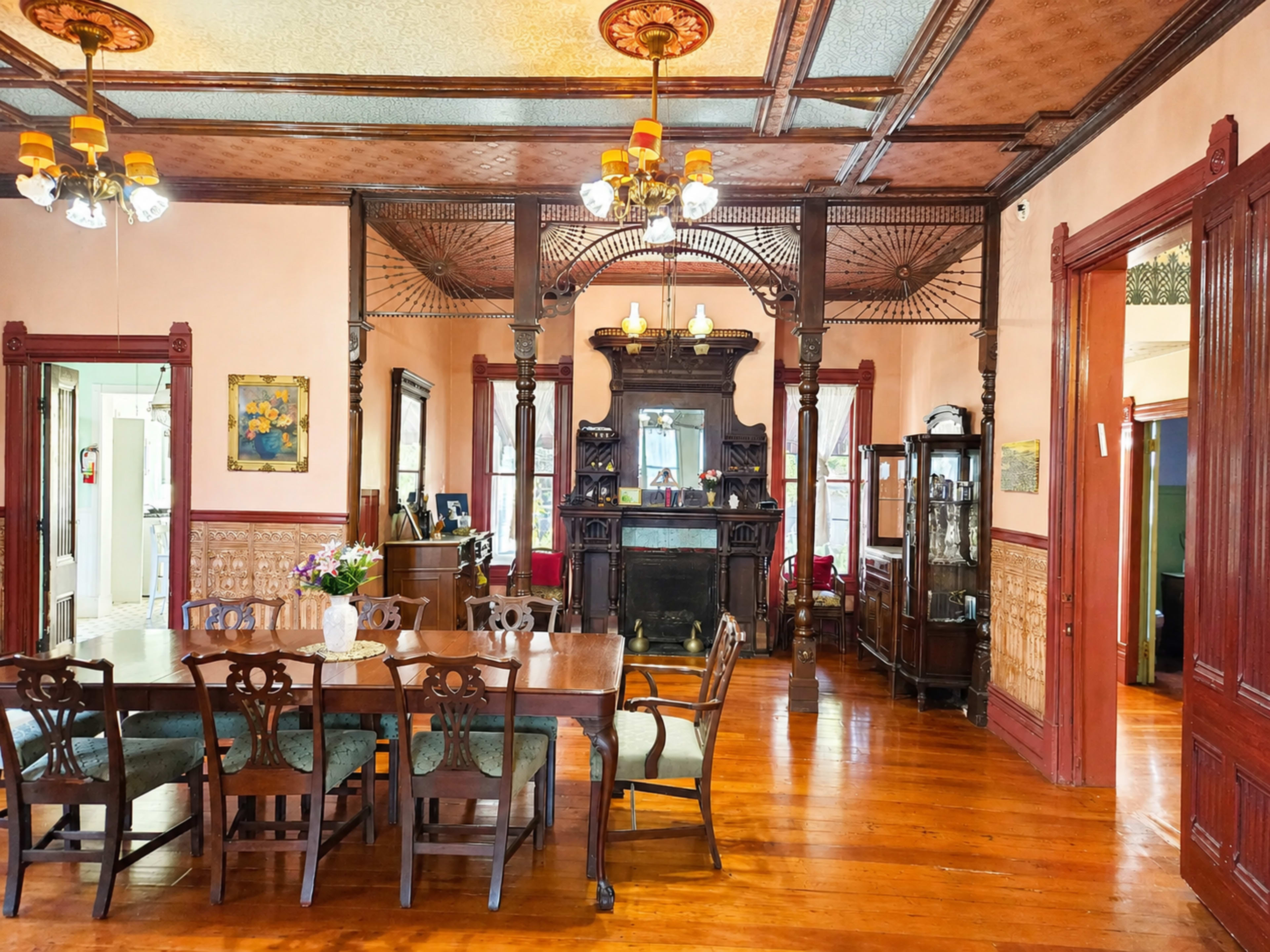 A spacious Victorian-style dining area features a long wooden table, ornate ceiling details, and a large fireplace surrounded by intricate woodwork.