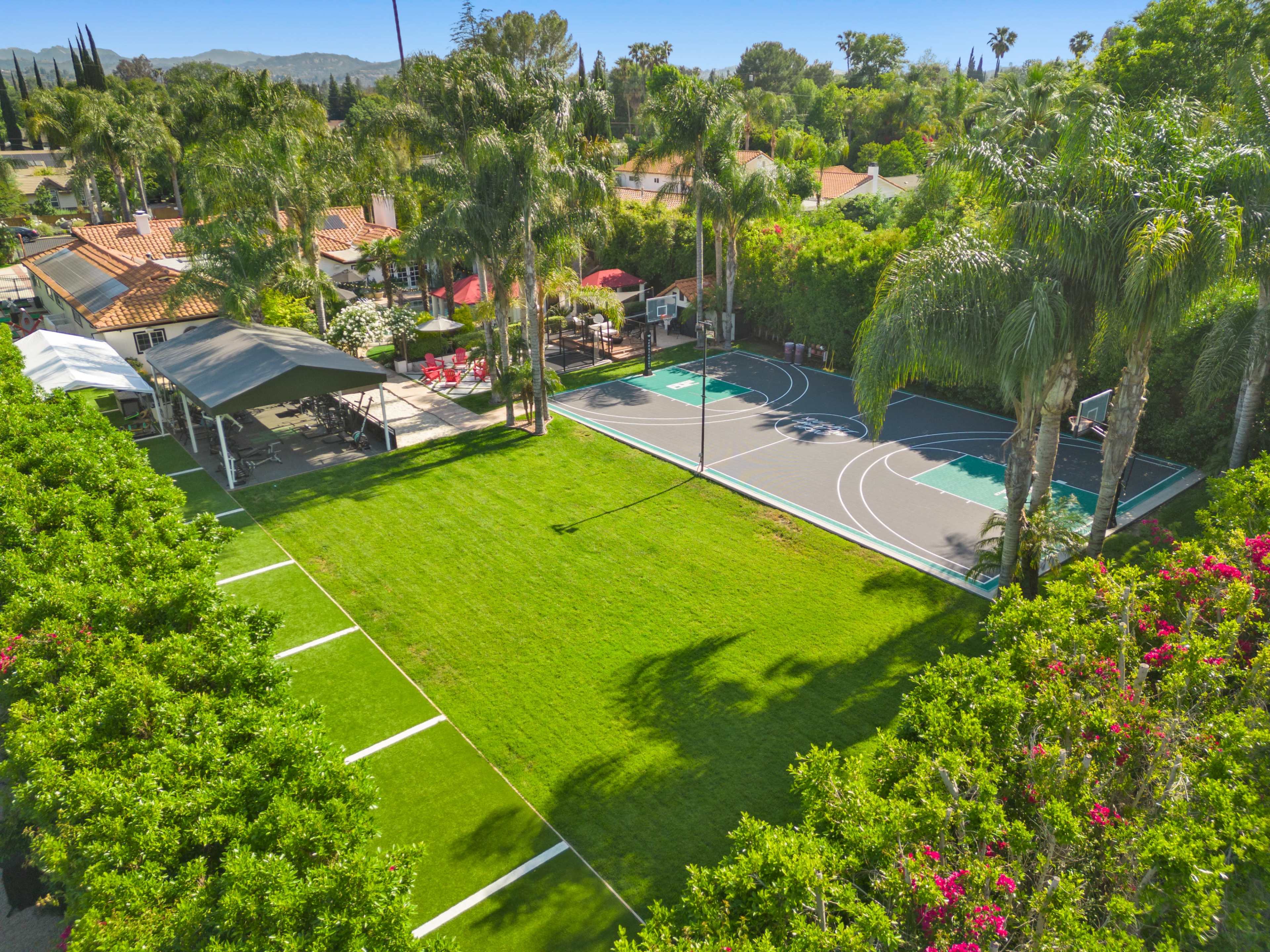 A spacious backyard featuring two basketball courts surrounded by lush greenery and landscaped areas.