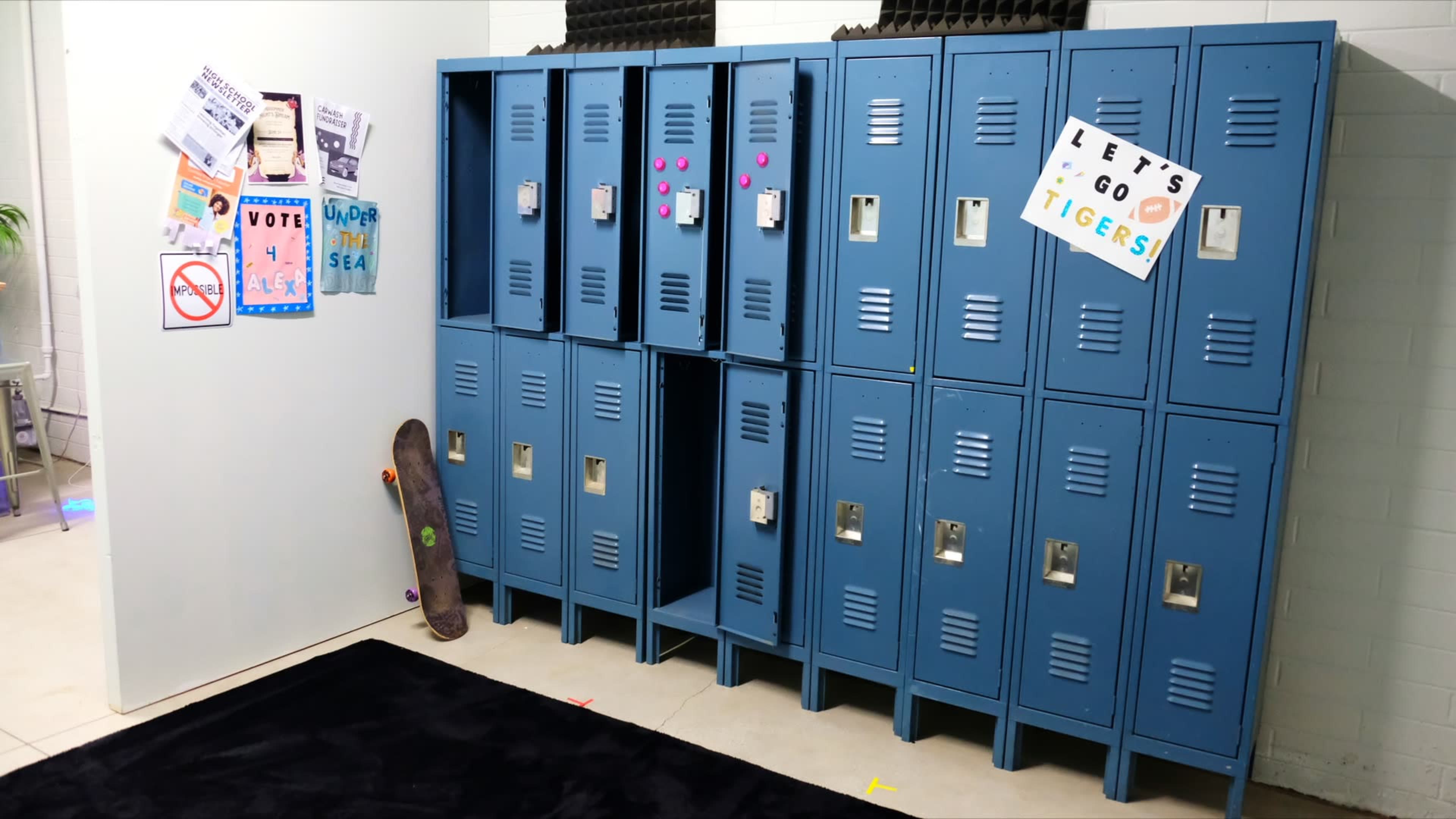 The image shows a row of blue school lockers, with one locker open, decorated notices on the walls, and a skateboard leaning against the lockers.