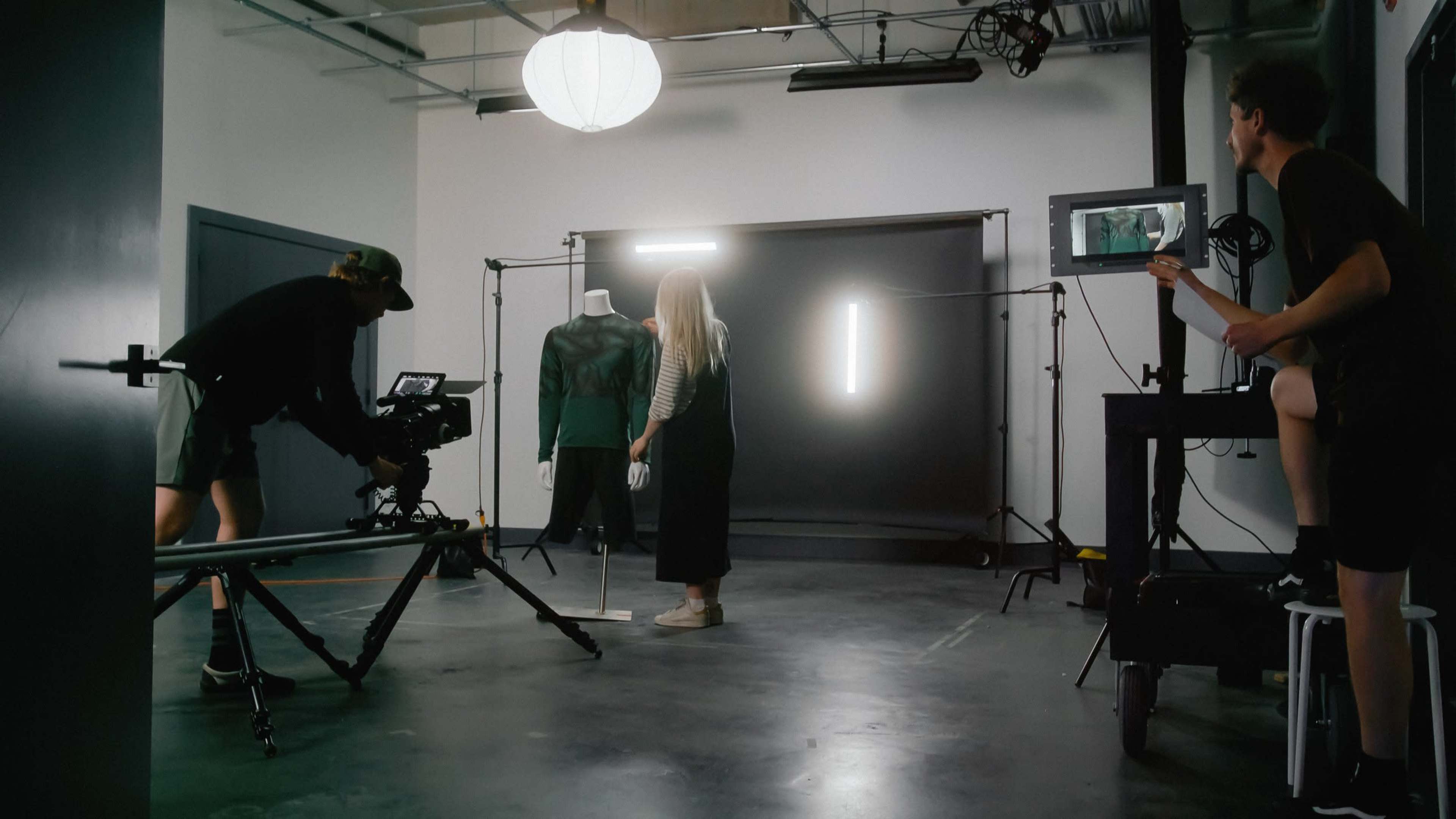 A film crew is setting up a video shoot in a studio with a mannequin and a backdrop.